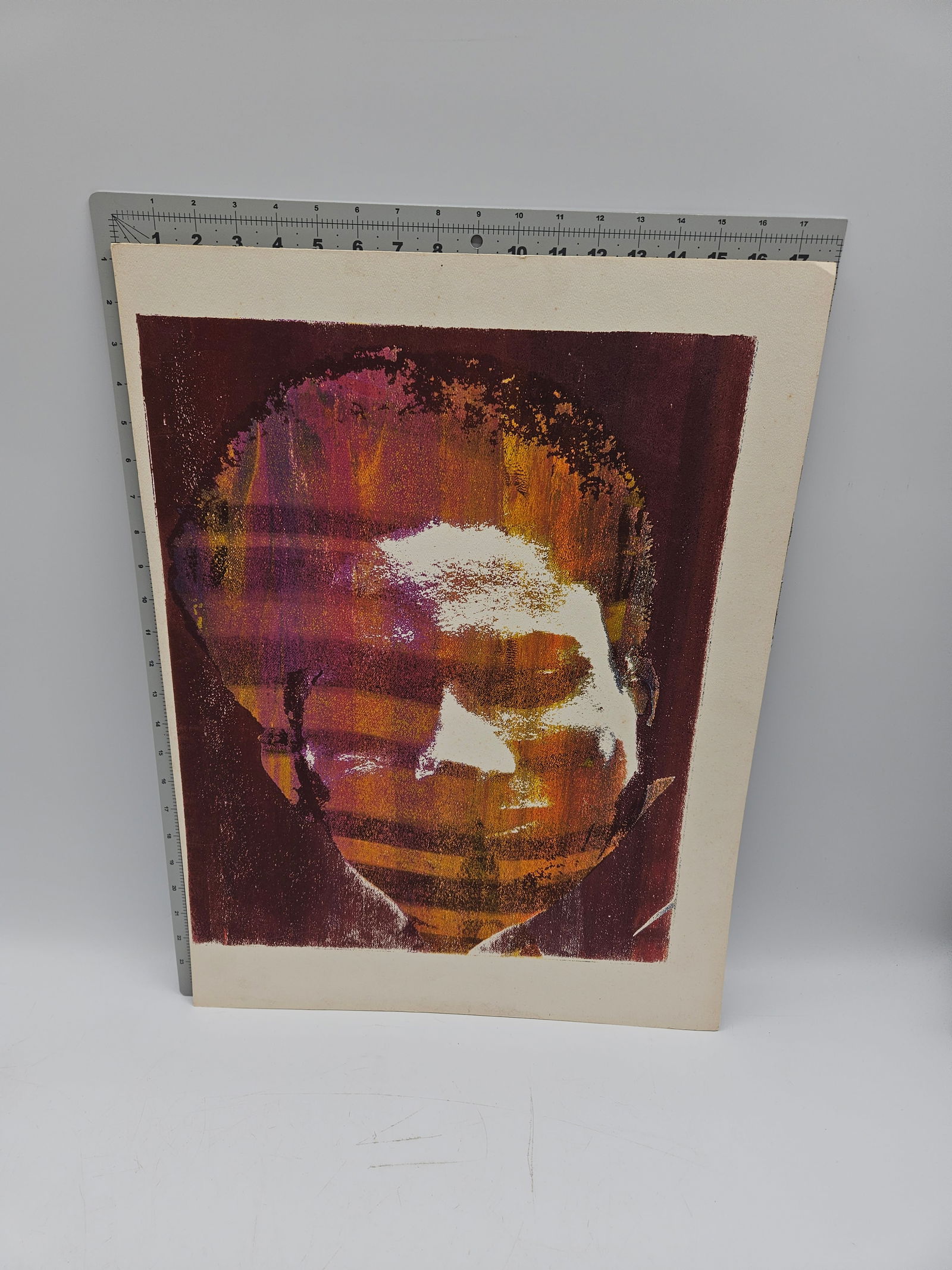 Abstract Portrait Print: Abstract portrait print featuring possibly Huey Newton rendered in shades of red, orange, and purple. Dimensions are approximately 24 x 18 inches.