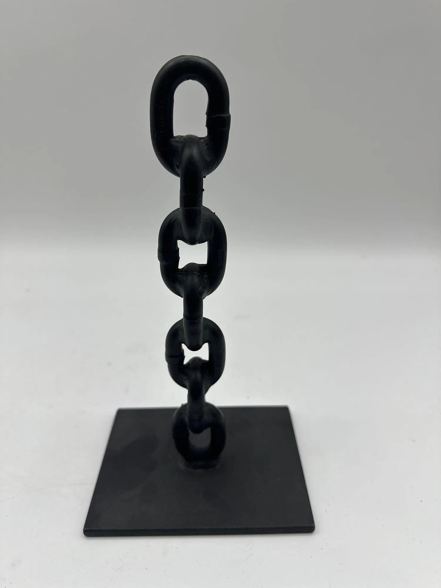 Gravity-Defying Iron Chain Sculpture: A black metal sculpture composed of welded iron chain links standing upright in a vertical position on a flat base, giving the illusion of floating or defying gravity. Often used as a conversation pie