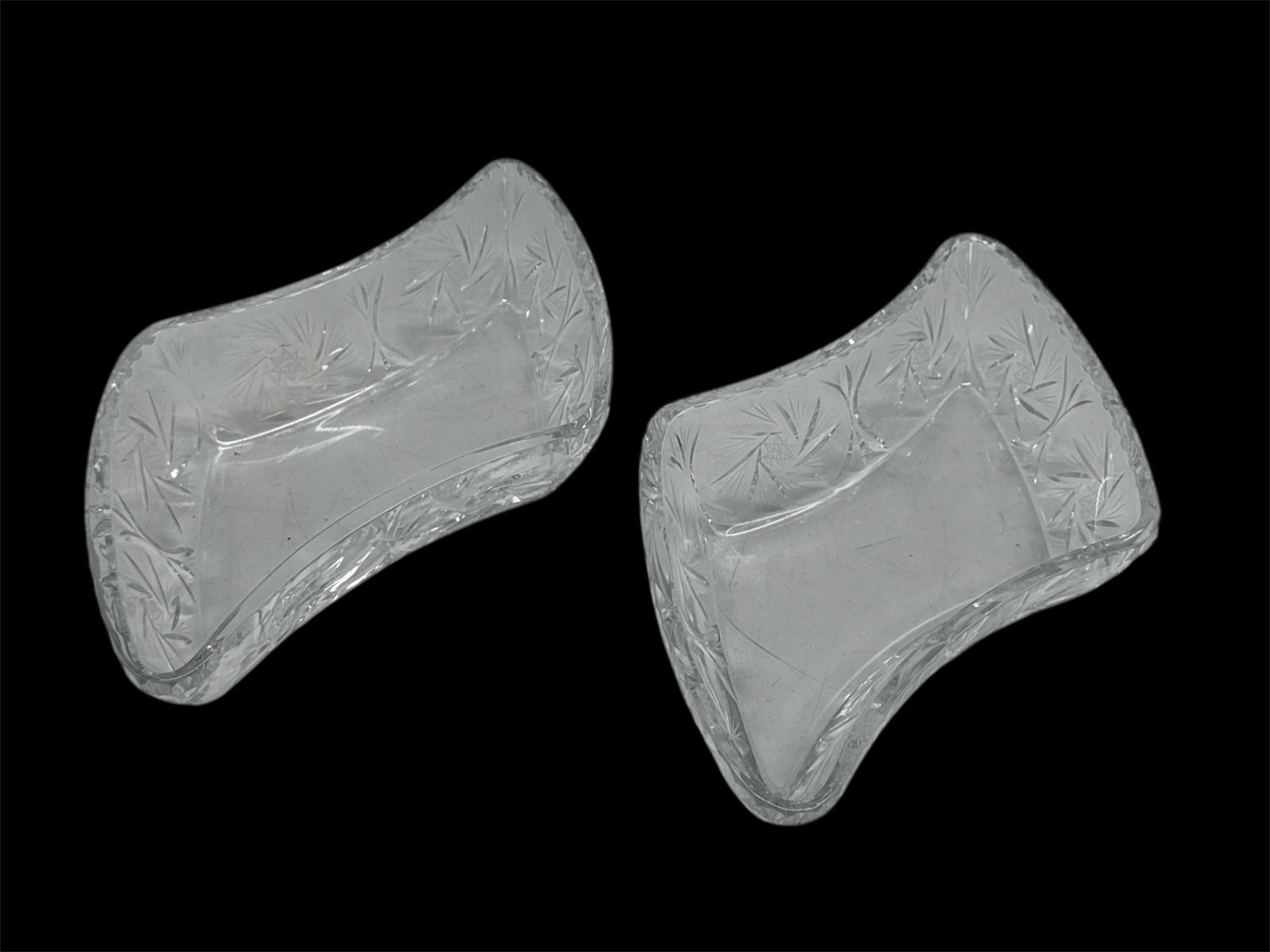 Pair of Cut Glass Console or Centerpiece Bowls: A pair of clear cut glass bowls featuring an elongated curved form with flared ends. Each piece is decorated with etched and cut floral and starburst motifs that enhance brilliance and light reflectio