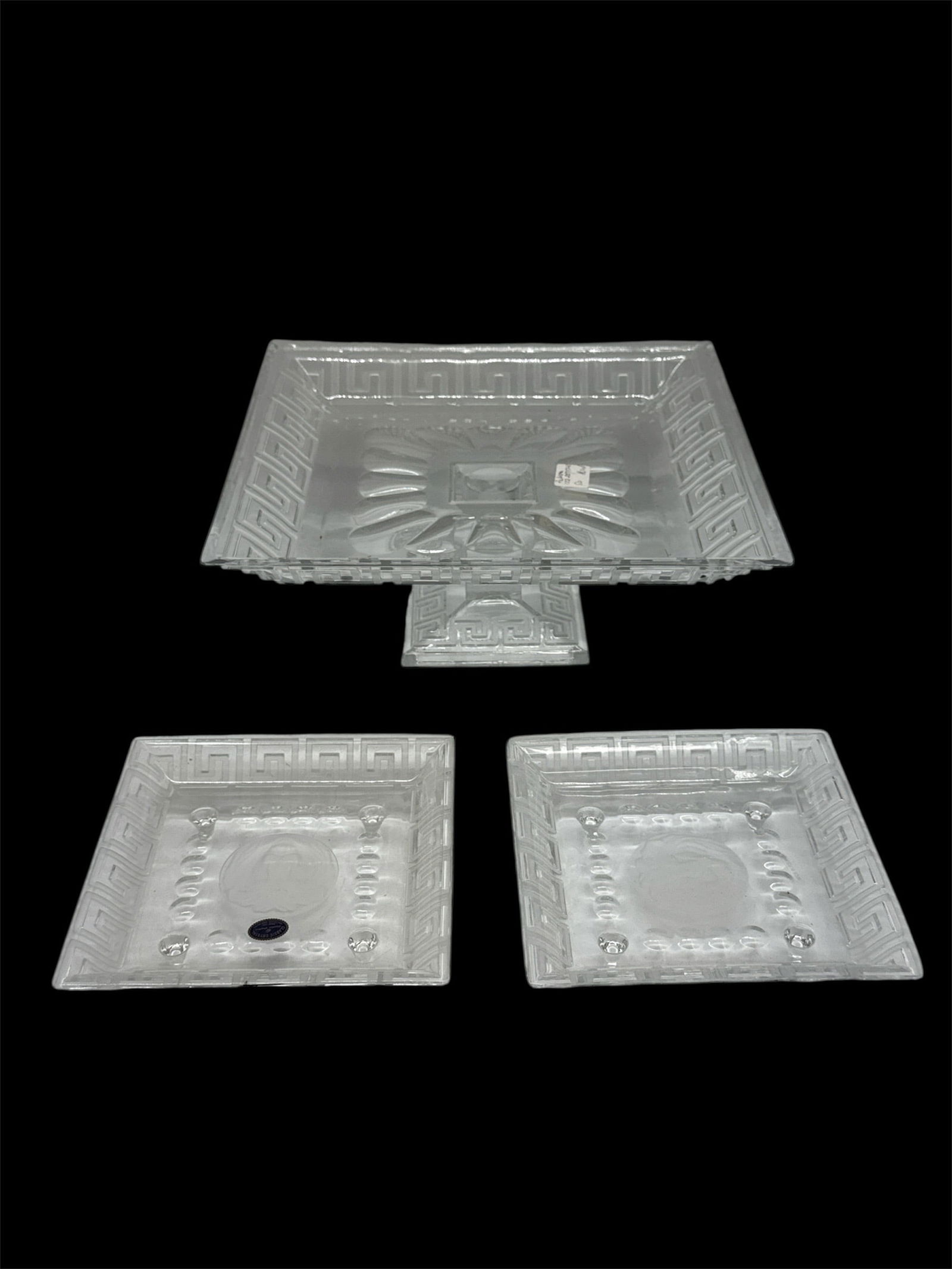 Three Piece Pressed Glass Serving Set with Pedestal Bowl: A three piece pressed glass serving set consisting of a square pedestal bowl and two matching smaller square dishes. Each piece features molded geometric and starburst patterns with textured borders