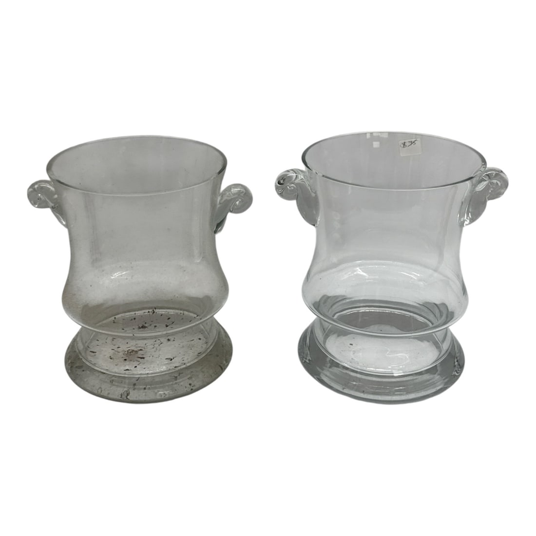 Pair of Clear Glass Cachepots with Scroll Handles: Classic pair of clear glass cachepots featuring gently flared cylindrical bodies and applied scroll side handles. Each piece rests on a broad circular foot, giving balance and presence to the form.