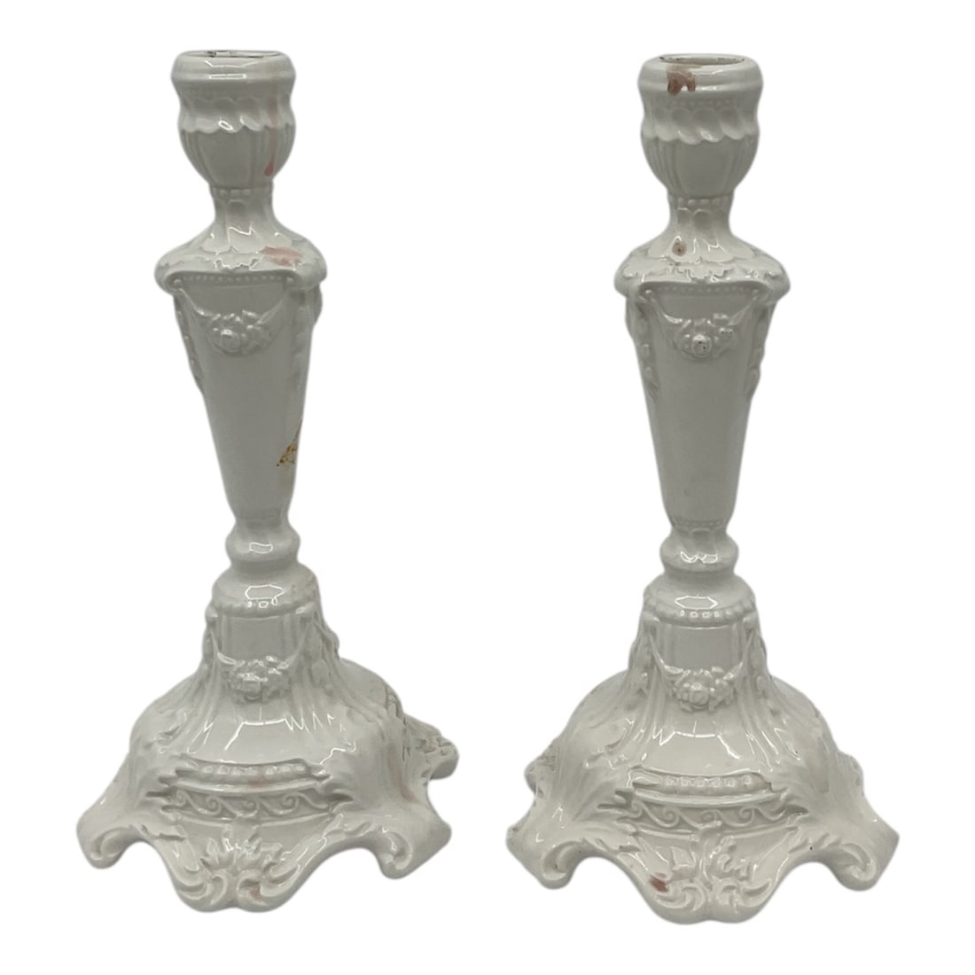 Pair of Capodimonte Style White Ceramic Candlesticks Made in Italy: Elegant pair of white ceramic candlesticks in the Capodimonte style, featuring ornate molded detailing with floral and scroll motifs. Each candlestick is raised on a decorative base with scalloped edg