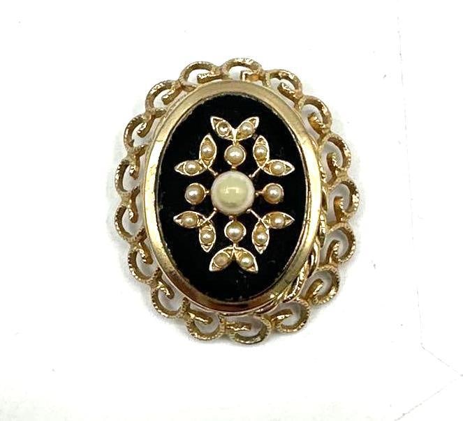Vintage Gold-Tone Filigree Brooch with Faux Pearls: Oval brooch featuring an ornate gold-tone filigree frame surrounding a central raised floral motif set with faux pearls. The background appears to be a painted or enameled surface in gray-blue tones,