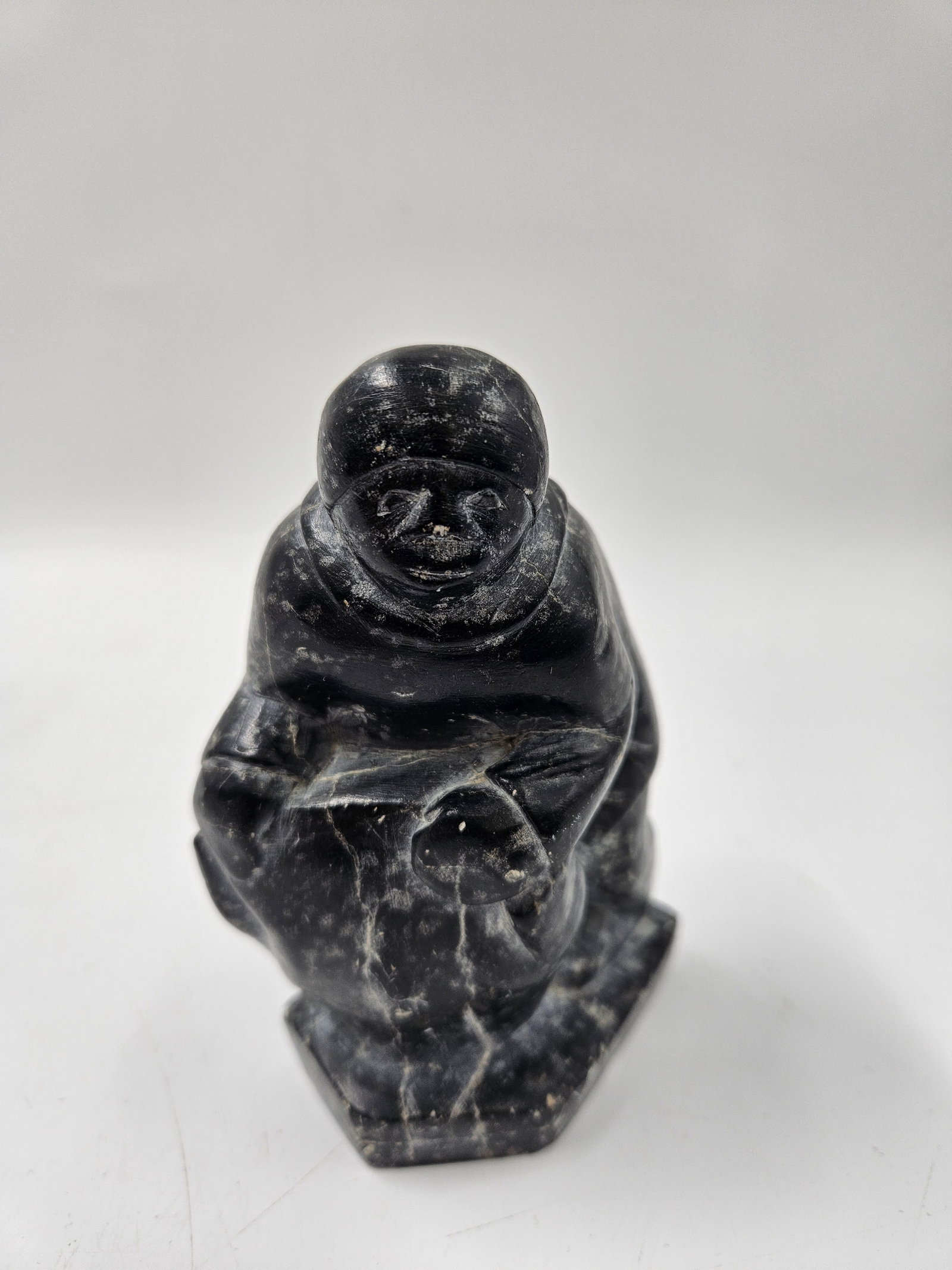 Inuit Eskimo Soapstone Carving: A hand-carved Inuit-style sculpture depicting an Eskimo figure in traditional clothing. The piece captures a moment of daily life with characteristic simplicity and detail common in Arctic Indigenous