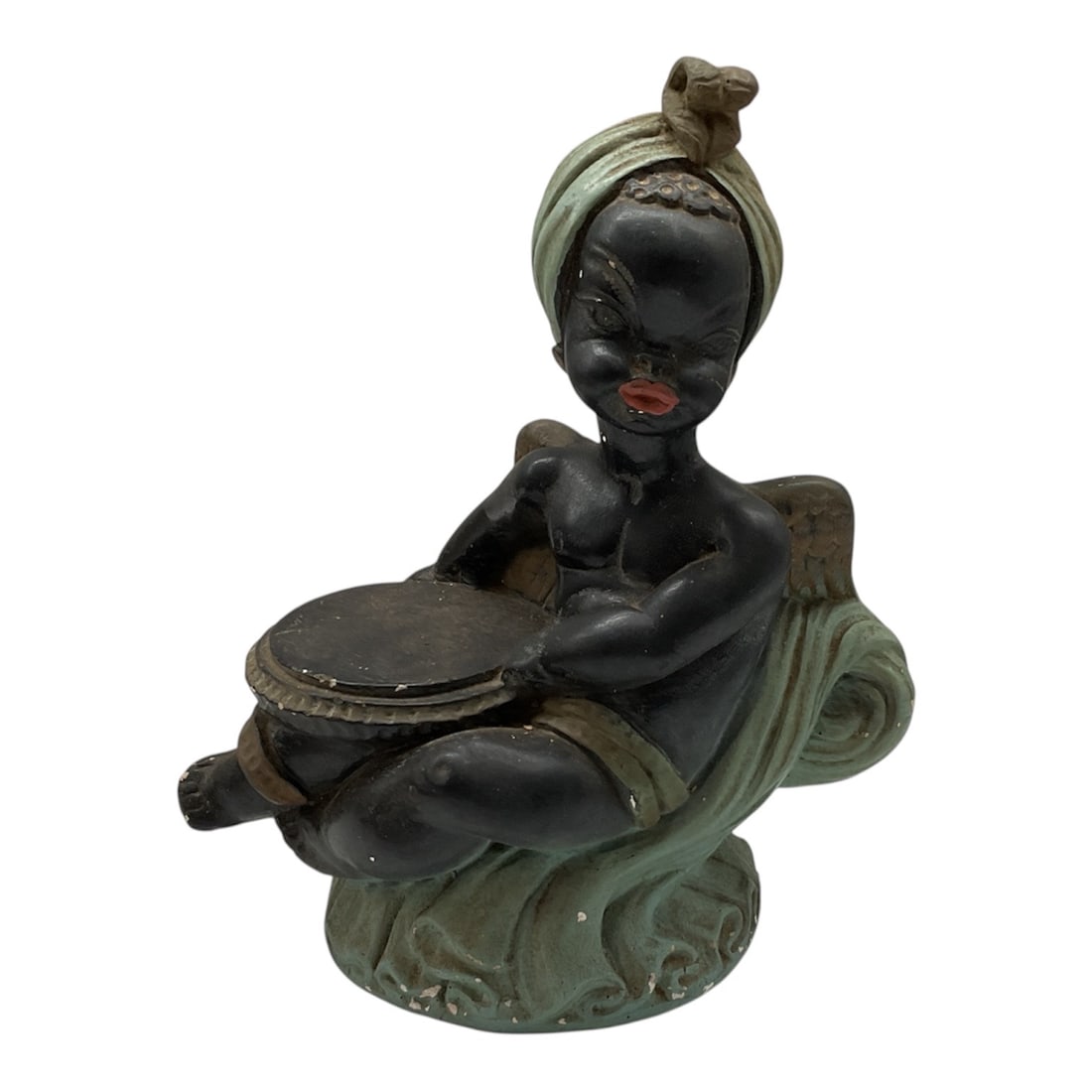 Black Americana Figural Drummer Boy Cast Metal Sculpture, 20th Century: A cast metal figural sculpture depicting a seated drummer boy in a stylized, folkloric form. The figure is shown playing a drum, with exaggerated features and a green patinated base suggesting a wave