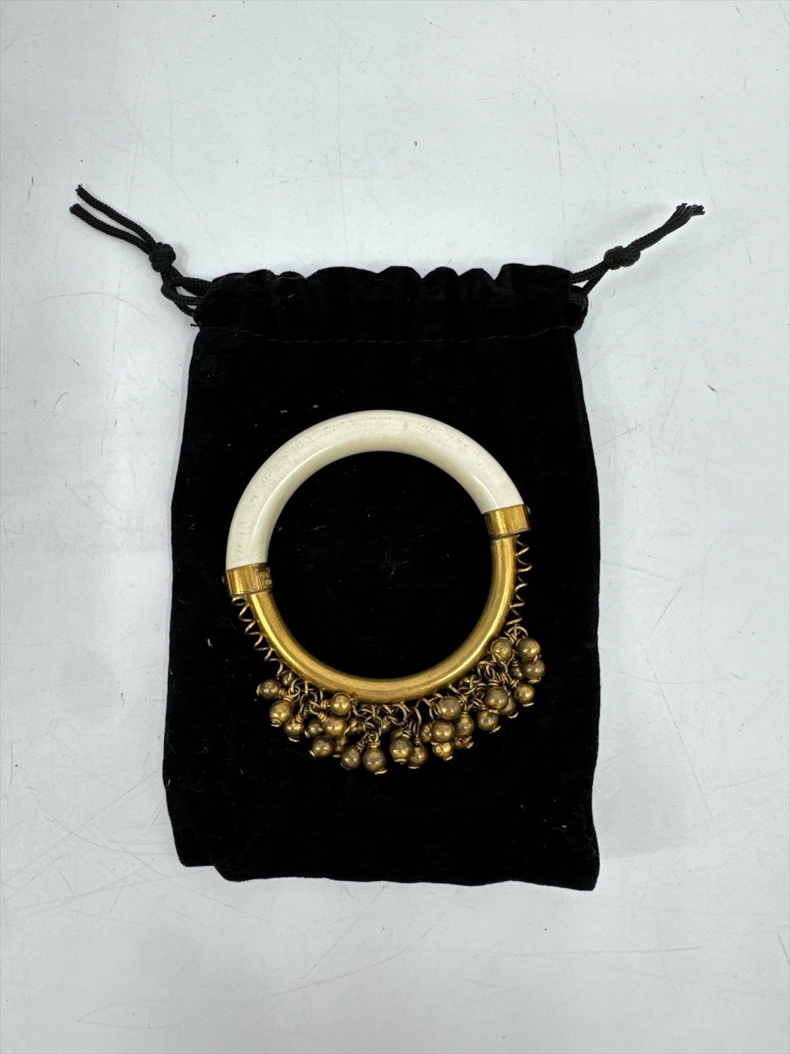 Elegant White and Goldtone Bangle Bracelet with Charms - Valentino: This stunning piece of fashion jewelry features a wide, smooth white or cream-colored band accented with gold-tone caps and dangling charms. The elegant design is reminiscent of high-end designer piec