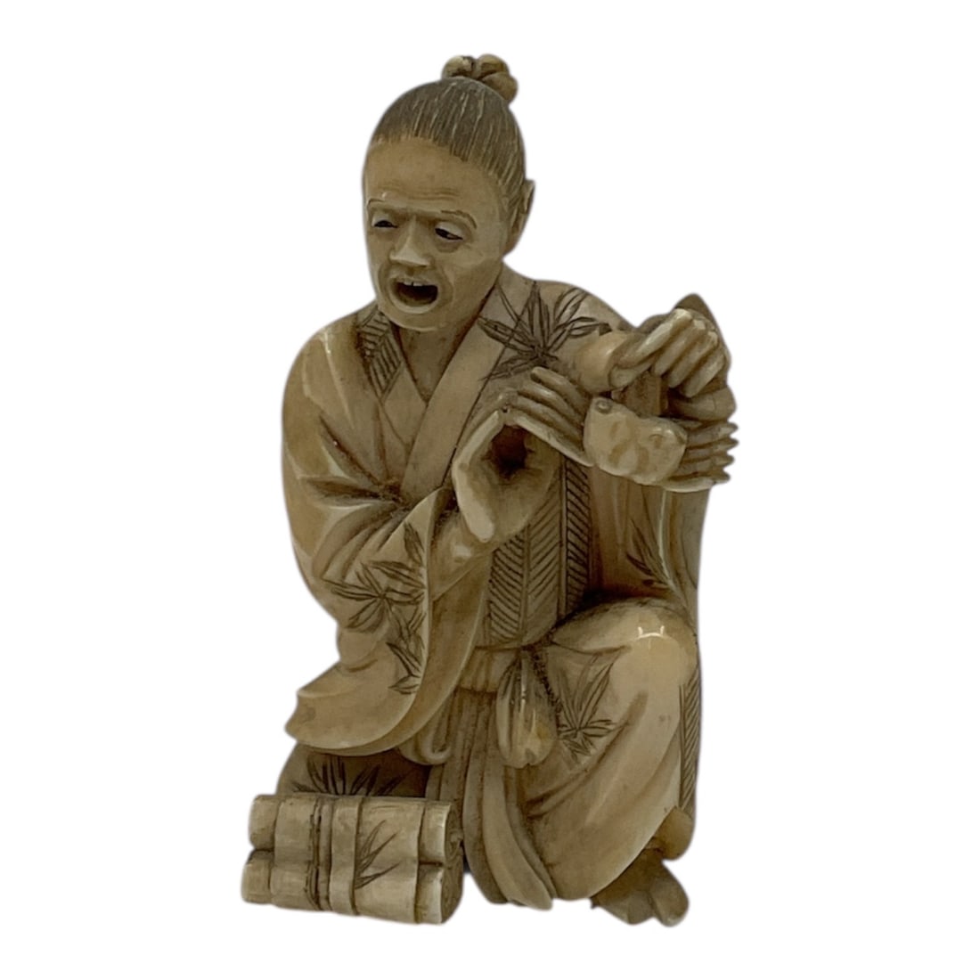 Carved Stone Figure of Seated Man with Bamboo Motif: Detailed carved stone figure depicting a seated man in traditional attire, holding an object in his hands. The figure is adorned with incised bamboo leaf decoration on the robe, adding texture and vis