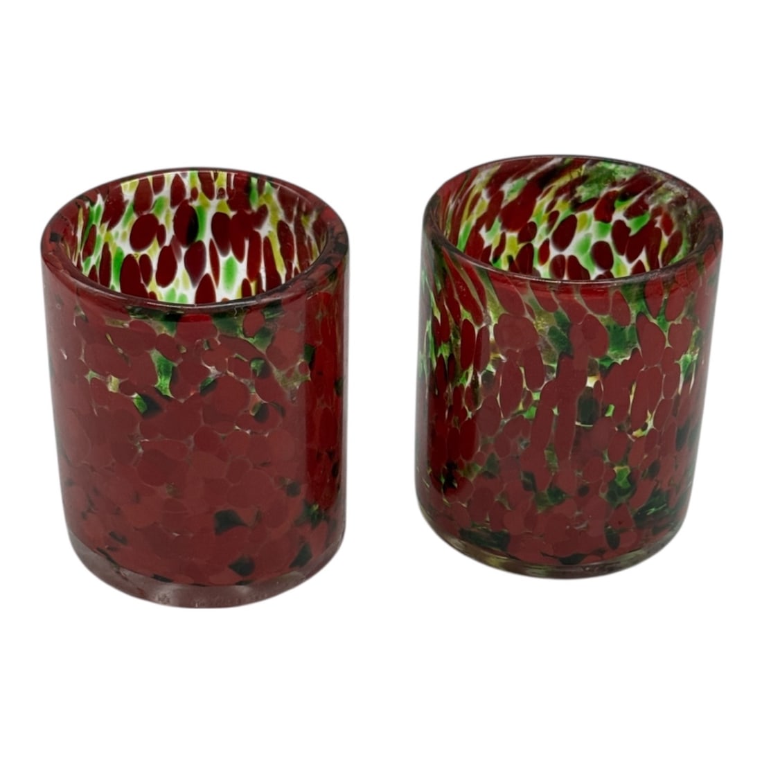 Pair of Red Spatter Glass Votive Candle Holders: Decorative pair of glass votive candle holders featuring a rich red ground with green and black spatter inclusions throughout. The colorful mottled pattern creates a striking glow when illuminated, ma