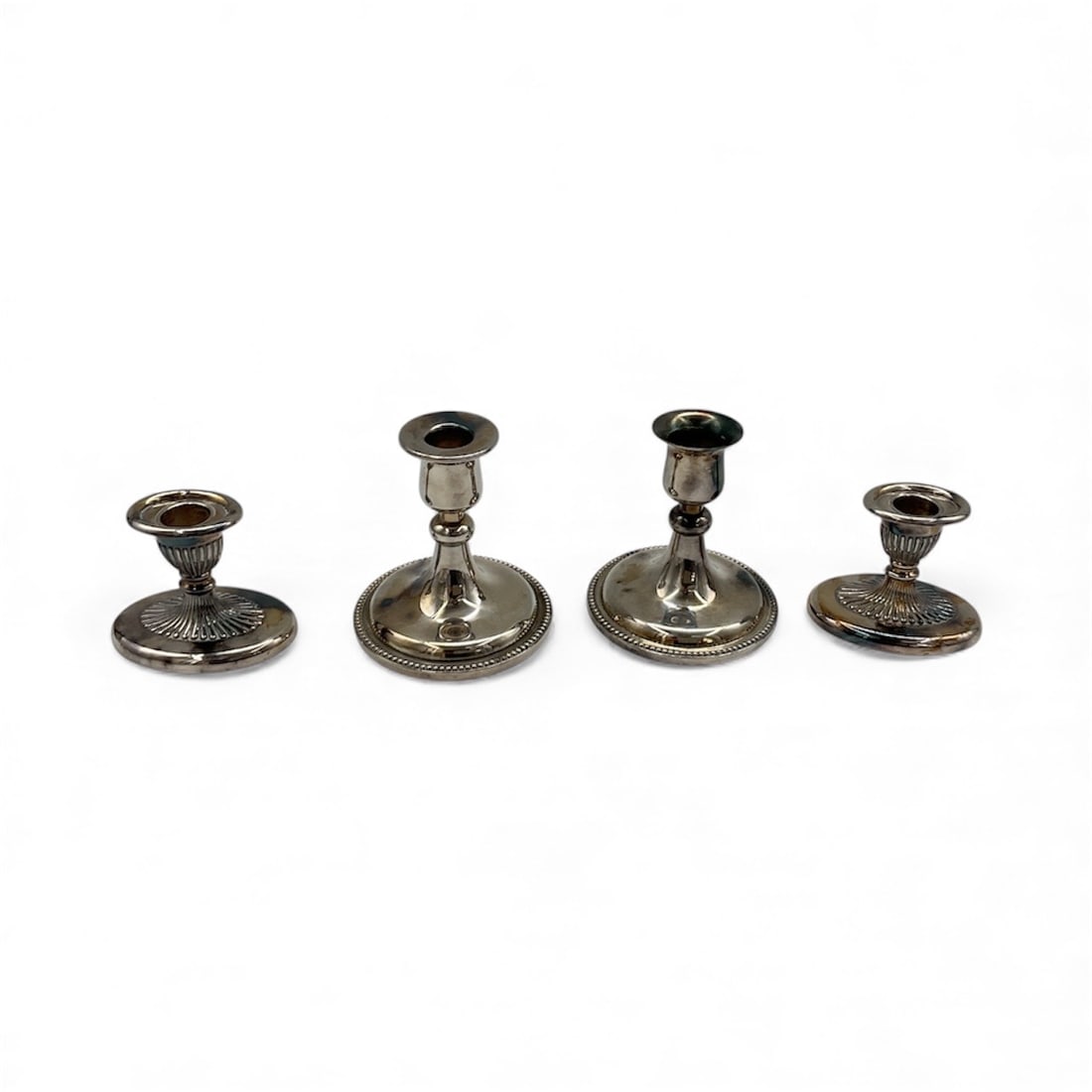 Vintage Candlesticks (4): Set of four assorted silver-tone candlesticks in graduated sizes, featuring classic round bases and traditional column forms. Ideal for decorative display or table settings. ranging H: 4 in