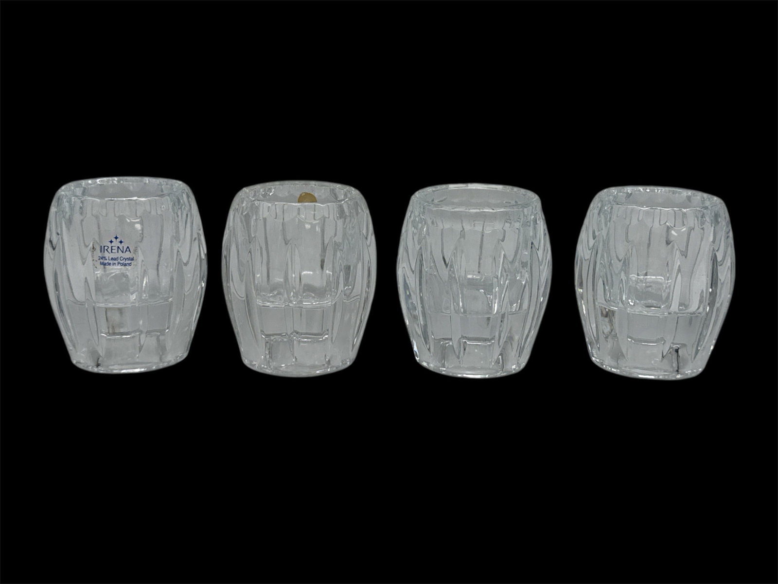 Set of Four Cut Glass Votive or Tumbler Cups: A set of four cut glass cups featuring deep geometric and vertical faceted patterns that enhance brilliance and light reflection. Each piece displays a rounded barrel form with substantial weight and