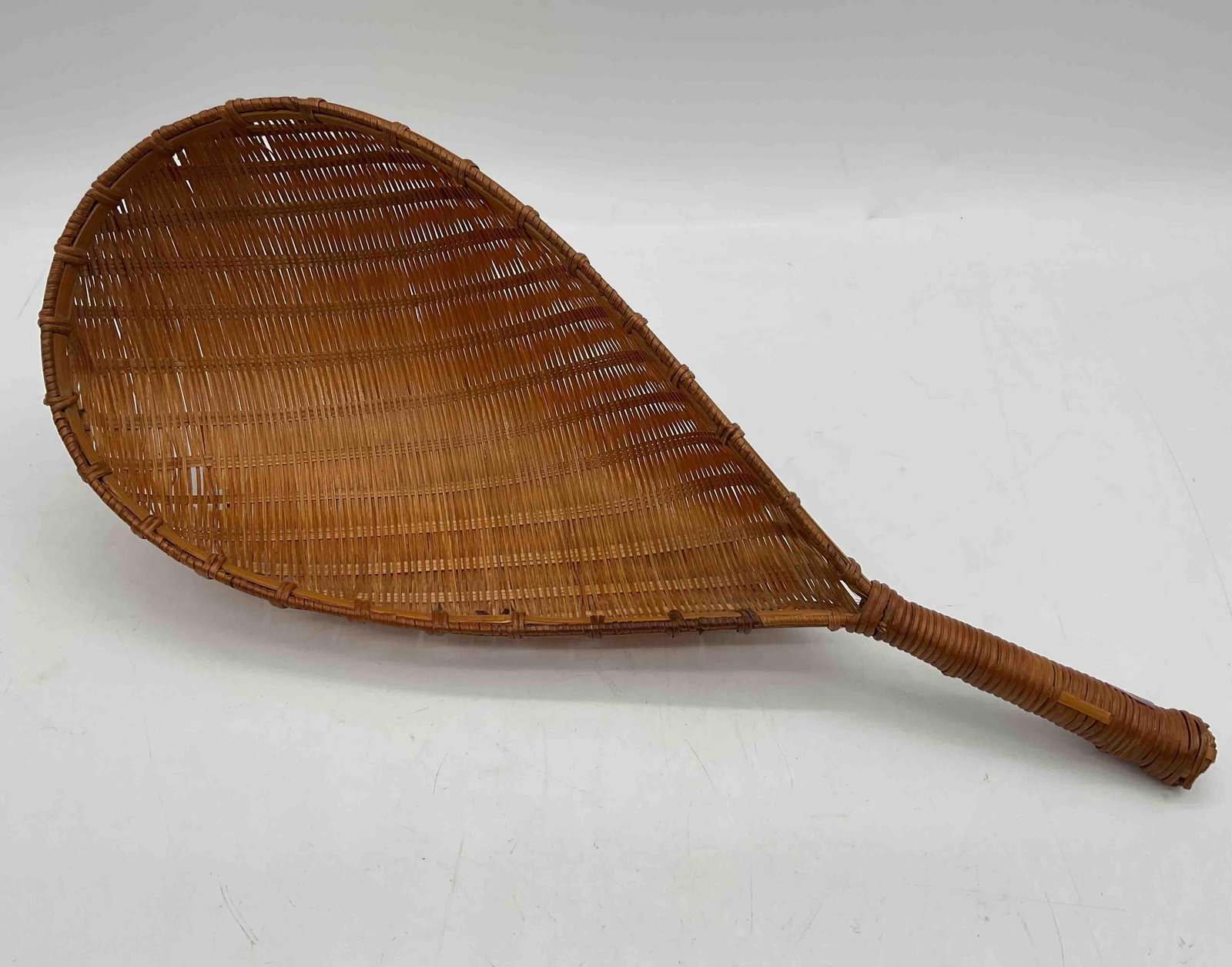 Vintage Handwoven Rattan Paddle Fan: Handcrafted woven fan with teardrop-shaped body and wrapped handle. Likely Native American or early colonial style, traditionally used for fanning fires or domestic purposes.Medium: Woven wood splints
