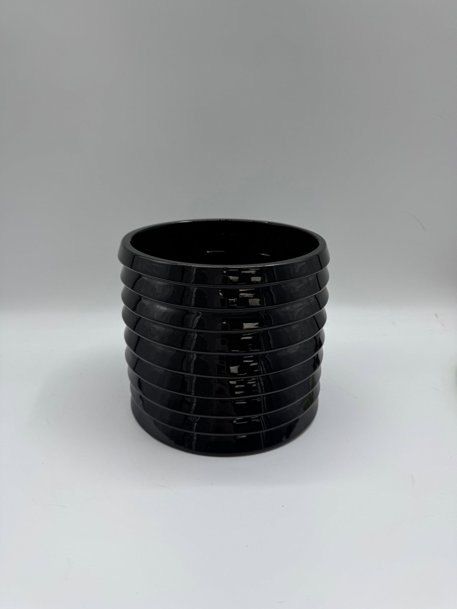 Black Ribbed Glass Vase: A modern black glass vase with a ribbed design. The vase has a cylindrical shape with a smooth interior and a textured exterior created by the evenly spaced ribs. A stylish decorative piece.