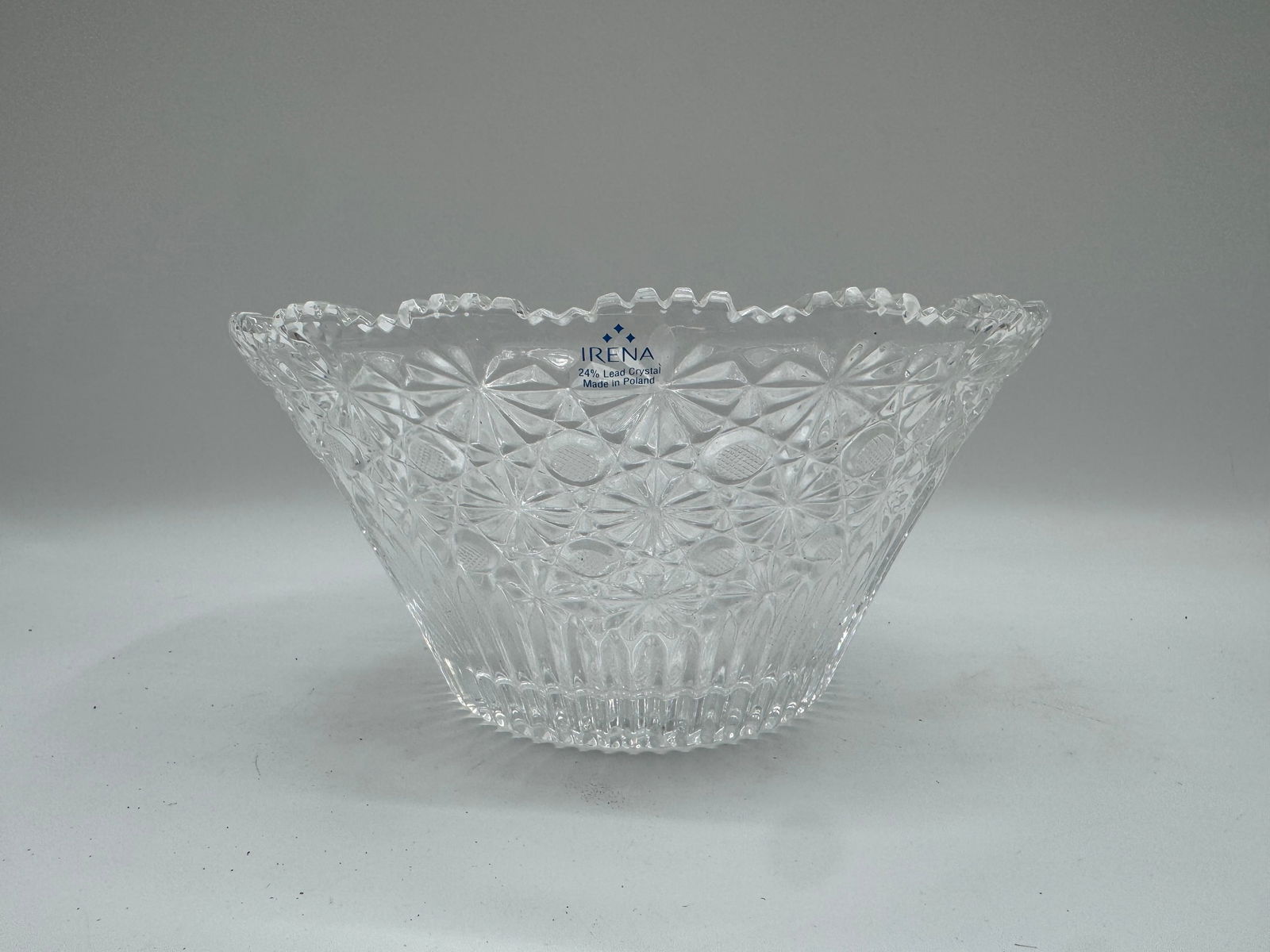 Rolina Clear Glass Bowl with Starburst Pattern: A clear glass bowl by Rolina, featuring a starburst pattern and a scalloped rim. The bowl has a round base and a flared shape. It is suitable for serving fruit, salads, or other decorative purposes.