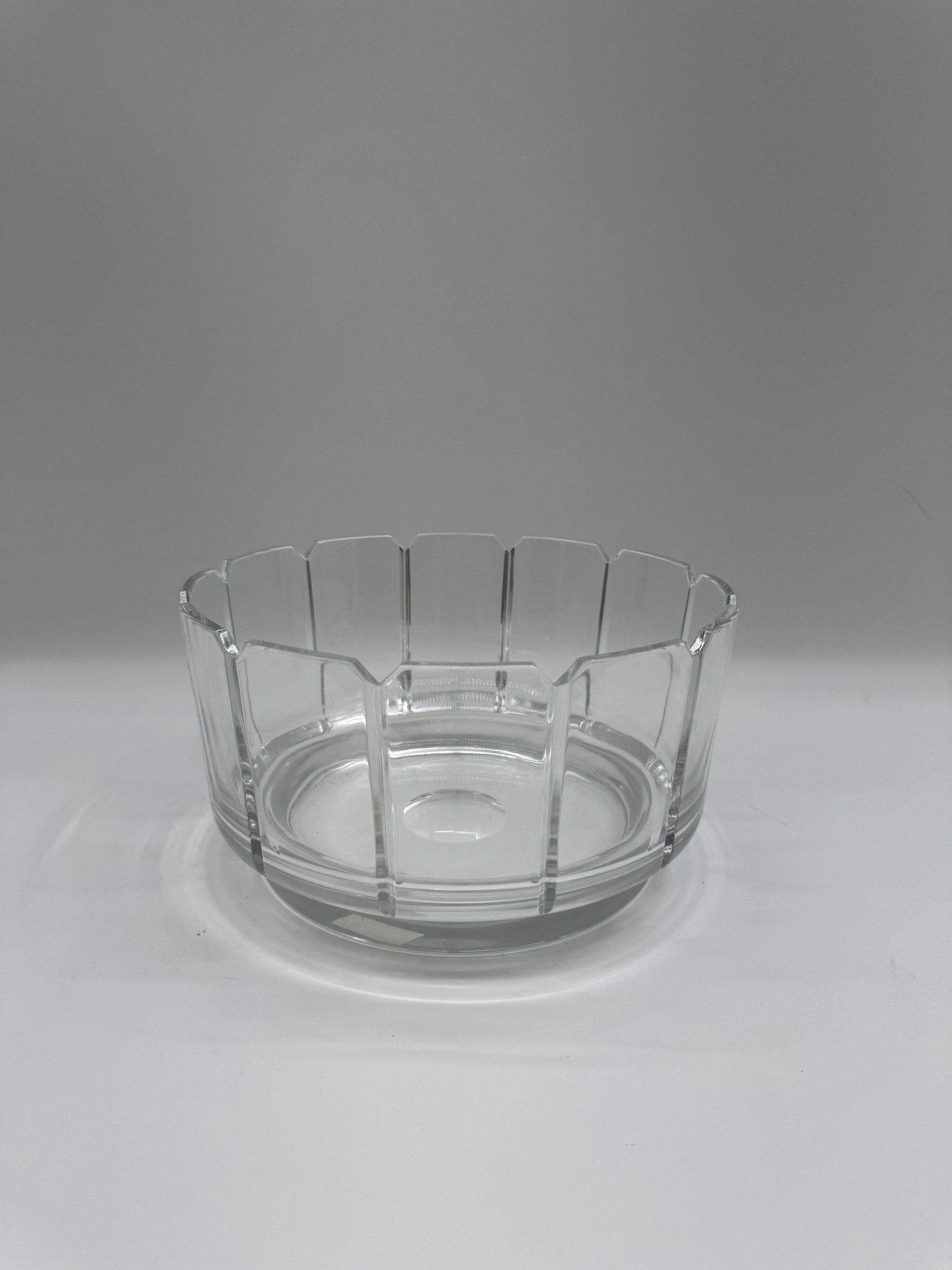 Clear Glass Bowl with Geometric Design: A clear glass bowl featuring a geometric design around the rim. The bowl has a circular base and a slightly flared shape. The design consists of vertical and slightly angled panels, creating a modern