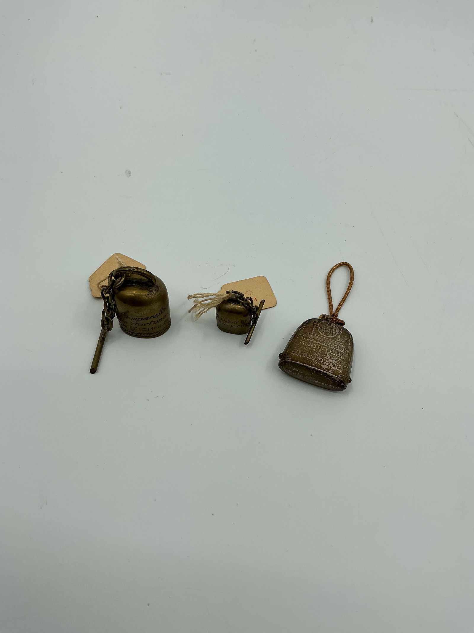 Three Assorted Metal Bells: Collection of three metal bells, each with a unique design and varying in size. The largest measures approximately 1 inch in height and 3/4 inch in diameter. Each bell includes a small chain or cord.