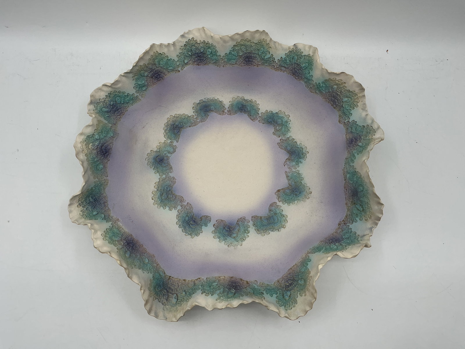 Large Studio Pottery Bowl, Signed M Jesco: Large studio pottery bowl with a ruffled edge and floral-like decoration in shades of green and purple. Signed on the bottom. Dimensions: H 4in x L 19in x W 19in.