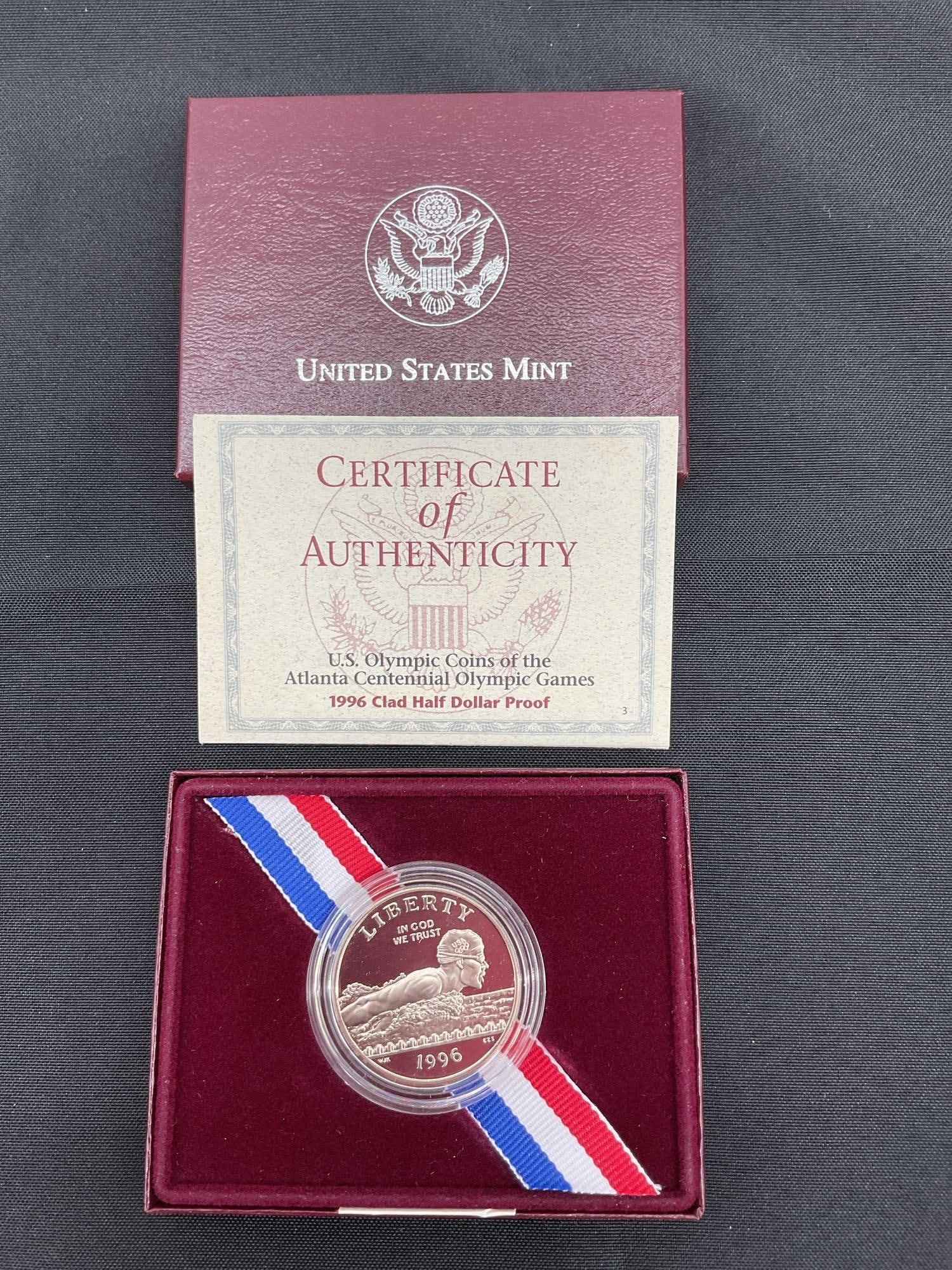 1996 U.S. Olympic Clad Half Dollar Proof coin: The image shows a 1996 U.S. Olympic Clad Half Dollar Proof coin, commemorating the Atlanta Centennial Olympic Games. The coin is presented in its original U.S. Mint packaging with a Certificate of Aut