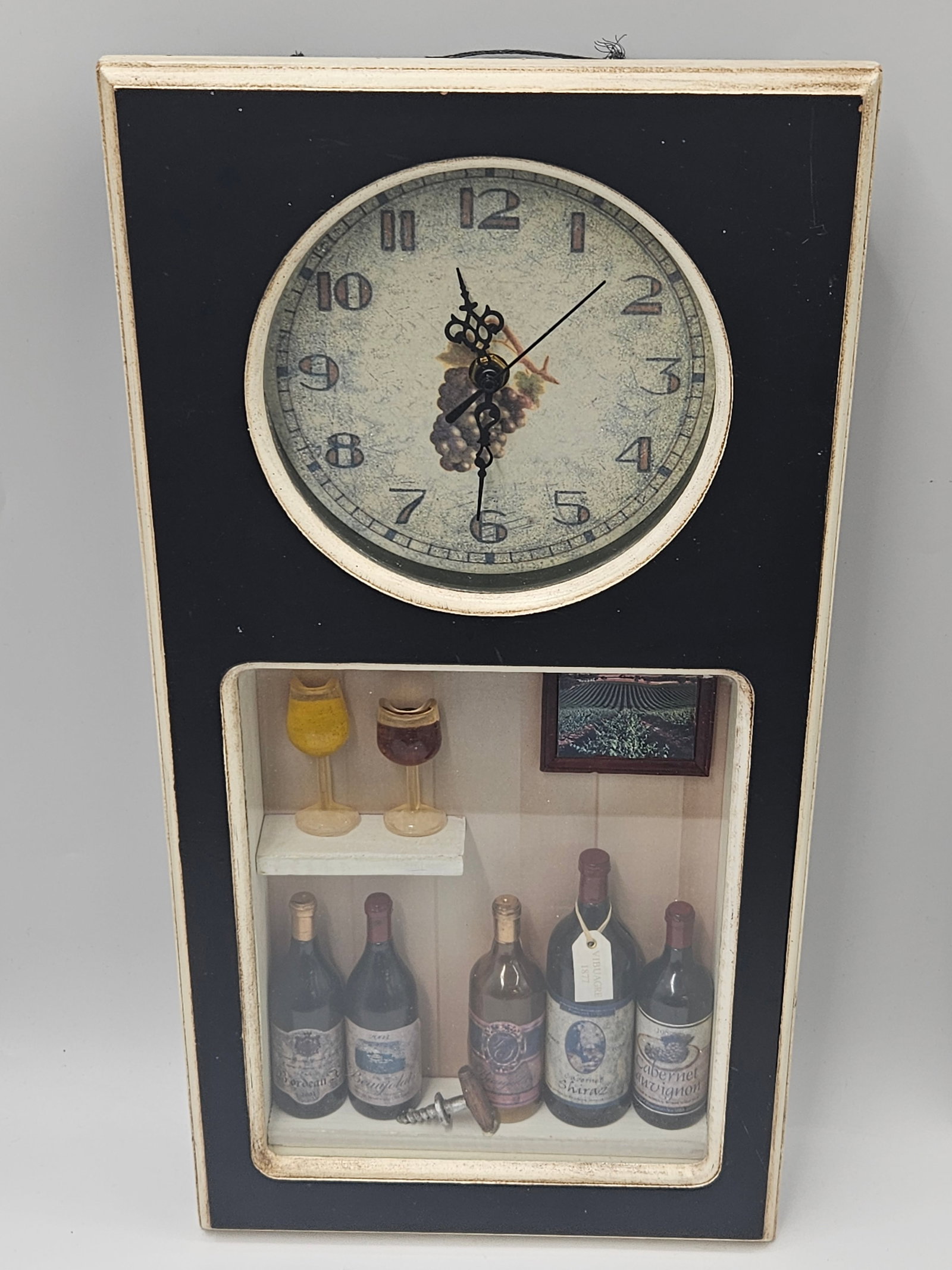 Wine Cellar Shadowbox Wall Clock: Decorative wall clock featuring a shadowbox display with miniature wine bottles, glasses, and framed art beneath the clock face. Combines functionality with rustic charm, ideal for kitchen, bar, or wi