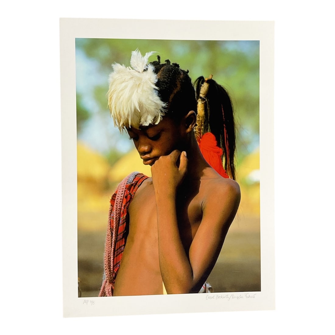 "Surma Boy with White Feathers, Ethiopia" by Carol Beckwith (USA, B.1945) and Angela Fisher: This striking color photograph features a young Surma boy from the Omo Valley in Ethiopia. He is depicted with a traditional headdress composed of large white feathers and a red tassel, complemented b