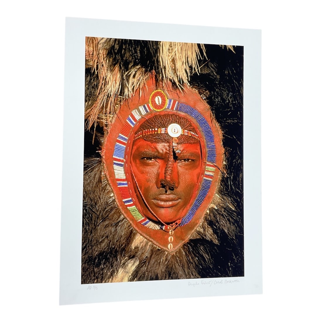 "Dinka Woman with Fish, South Sudan" by Carol Beckwith (USA, B.1945) and Angela Fisher (Australia,: This color photograph captures a Dinka woman in South Sudan, balancing a large fish on her head. The subject is adorned with traditional beaded necklaces and red pigment on her skin, set against a dee