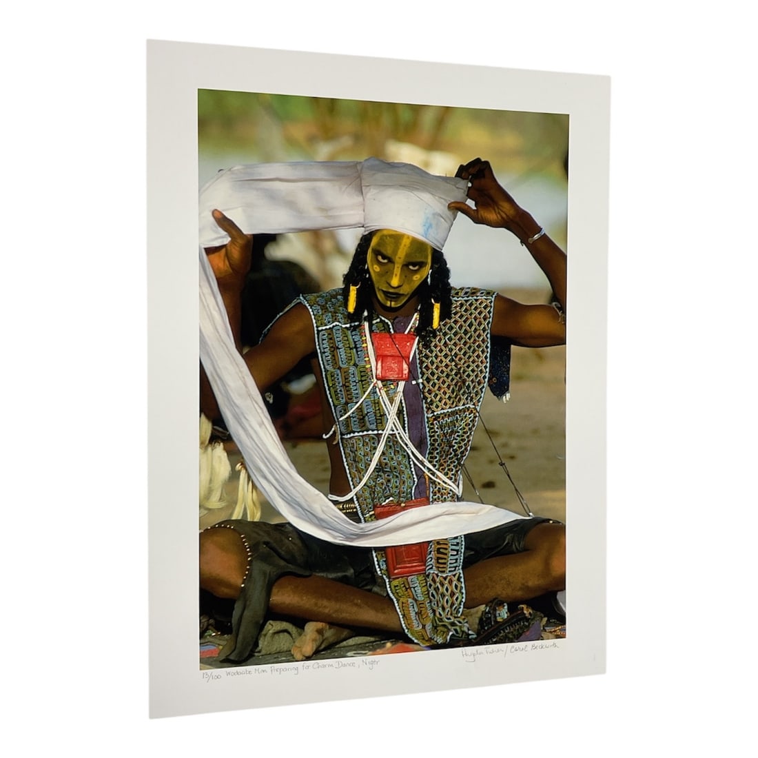 "Himba Wedding Guest, Namibia" by Carol Beckwith (USA, B.1945) and Angela Fisher (Australia, B.1947): This color photograph depicts a young Himba woman in Namibia, identified as a wedding guest. She wears the traditional erembe headdress of a married woman and a prominent white conch-shell pendant, an