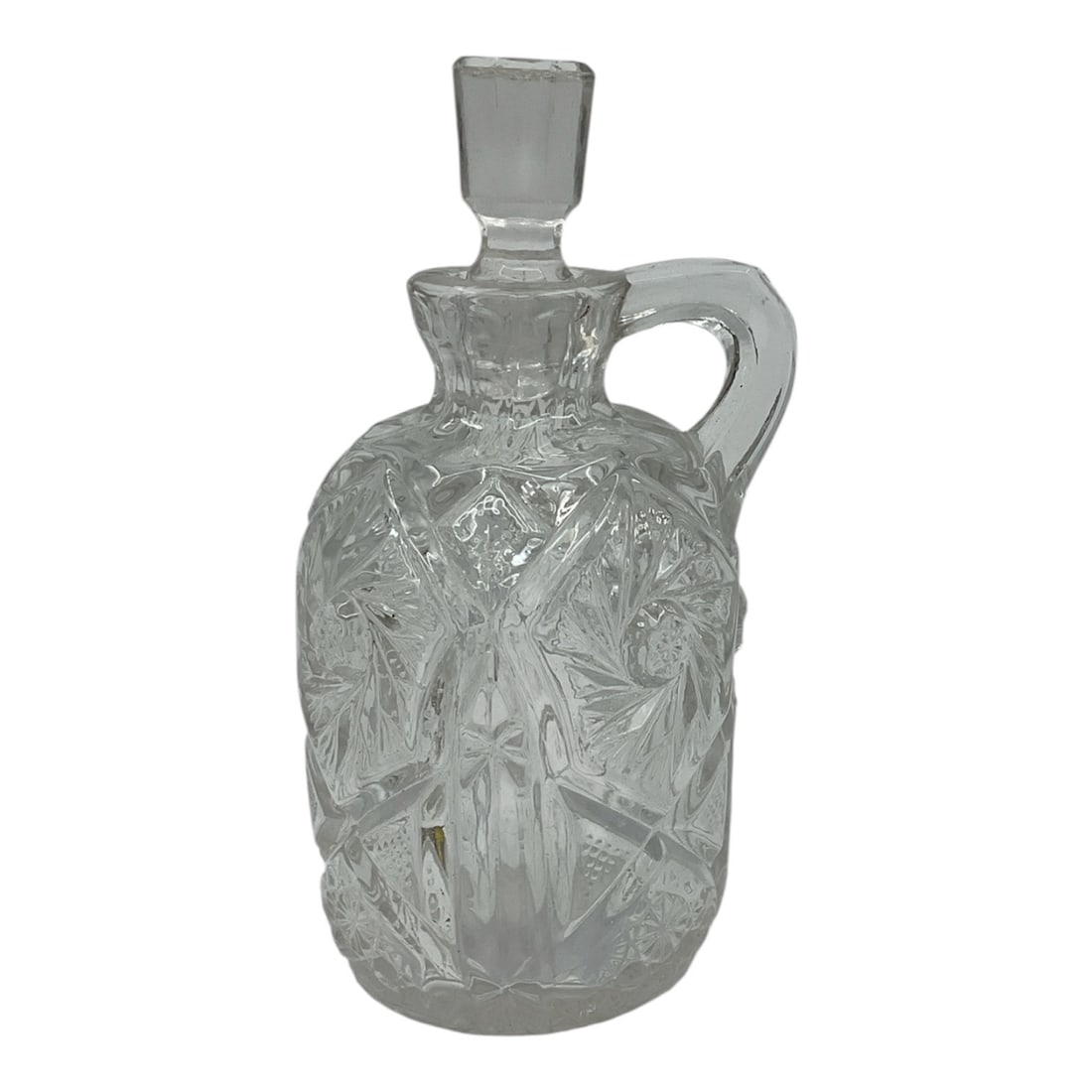 Cut Glass Cruet with Stopper: A decorative cut glass cruet featuring intricate starburst and geometric patterns throughout the body. The form includes a single applied handle and a fitted faceted stopper, giving it both functional