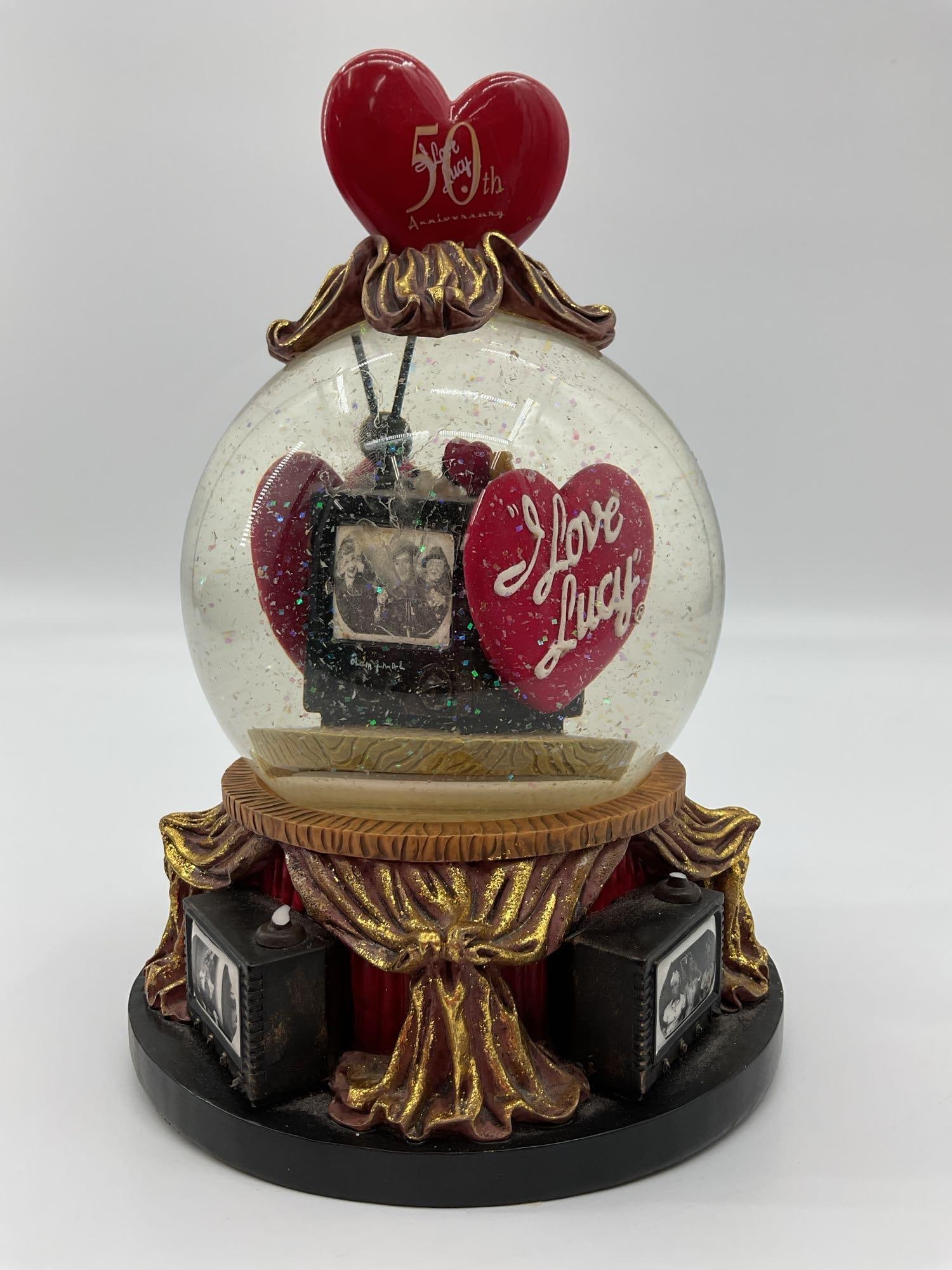 I Love Lucy Snow Globe: Vintage style snow globe featuring a heart with I Love Lucy text in front of a retro television set. The base is designed with golden curtains and old fashioned TV sets displaying black and white