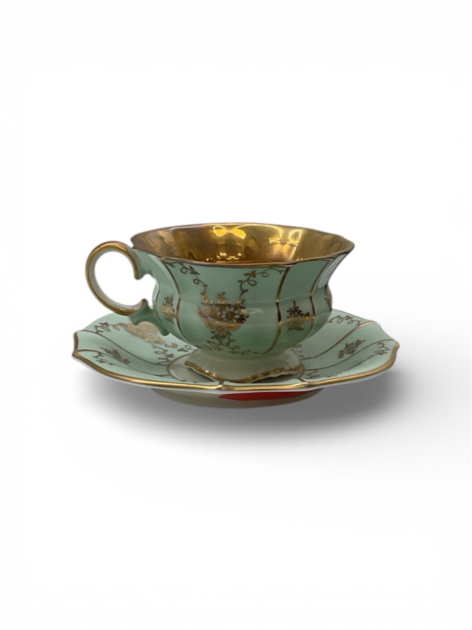 Made in Germany Porcelain Demitasse Cup and Saucer with Gilt and Scenic Decoration: This porcelain demitasse cup and saucer set was made in Germany and features a soft green ground decorated with scenic cartouche imagery and ornate gilt accents. The cup displays a white exterior band