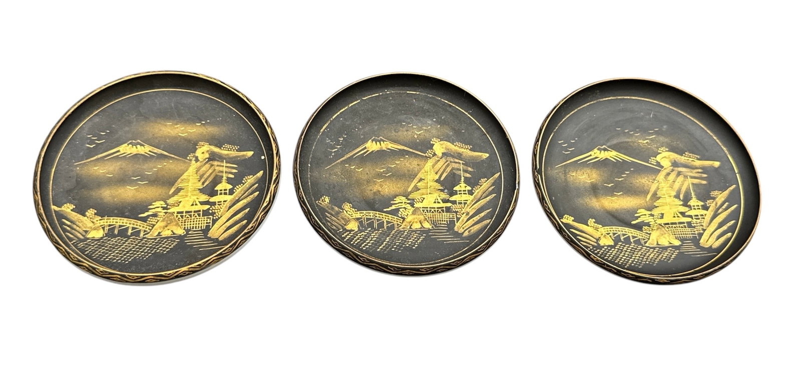 Set of Three Koshida Japan Gold Decorated Plates with Pagoda Landscape Scenes: This set of three decorative plates by Koshida Japan features finely detailed gilt landscape scenes depicting traditional pagodas, bridges, and mountainous settings against a dark ground. The