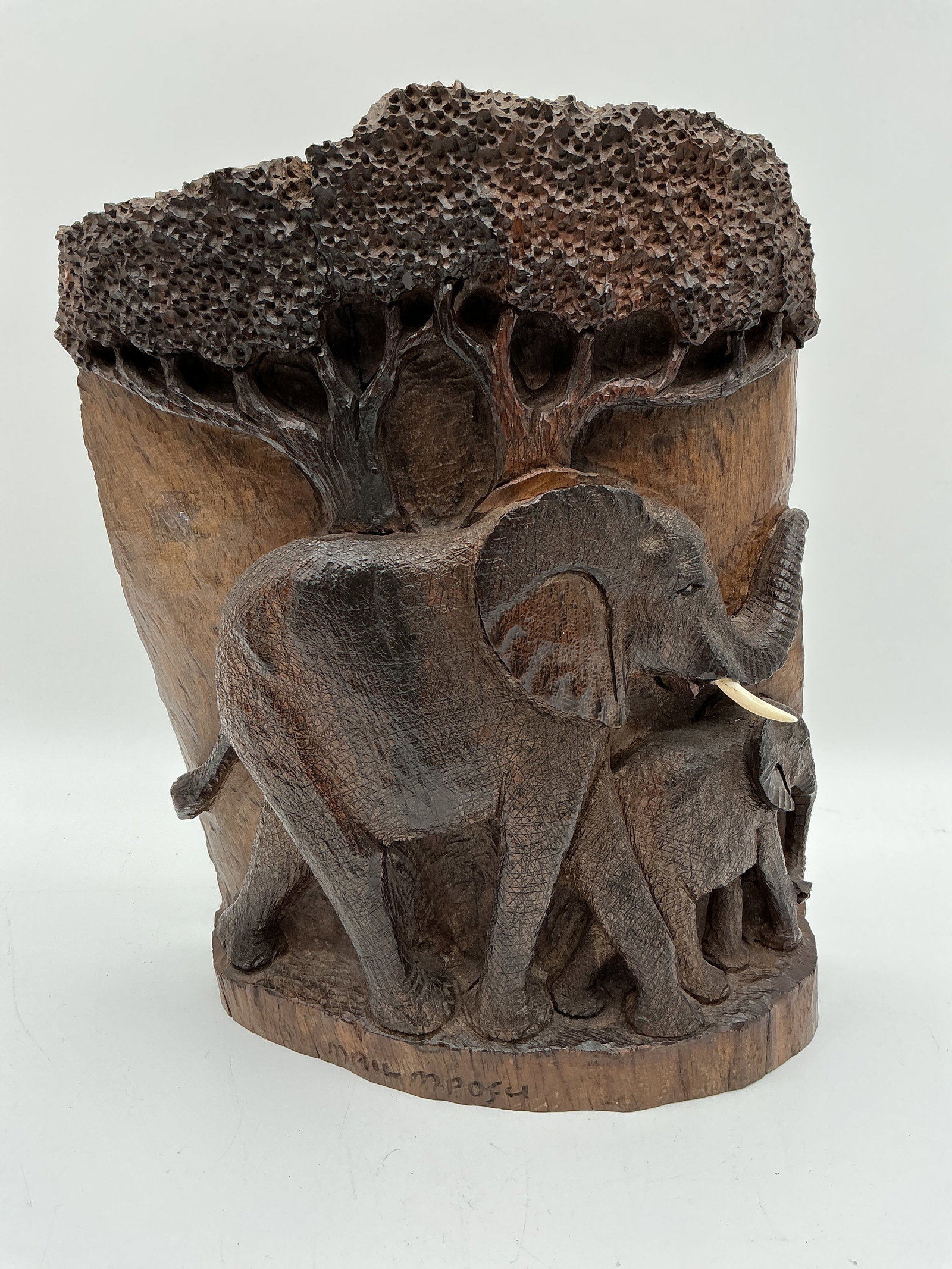 Hand-Carved Elephant Family Sculpture by Mpofu: Finely detailed African hardwood carving signed by artist Mpofu, depicting a mother elephant and calf beneath a tree. The piece showcases intricate texture work on the elephants’ skin and