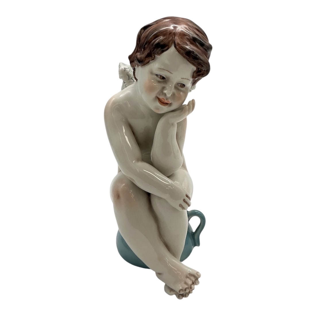 Porcelain Cherub Angel Figurine Seated on Pitcher - Grupo Galos: A glazed porcelain figurine depicting a seated cherub with wings, shown in a contemplative pose resting its head on one hand. The figure is modeled with soft naturalistic features