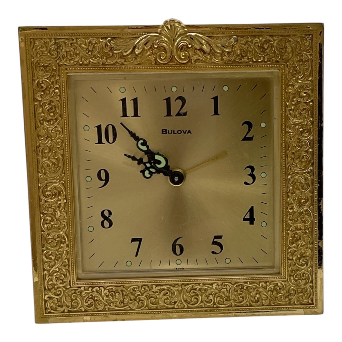 Bulova Brass Desk Clock: A vintage Bulova desk clock featuring an ornate brass-tone square case with elaborate repoussé-style floral and scroll decoration. The clock face displays Arabic numerals with decorative black 