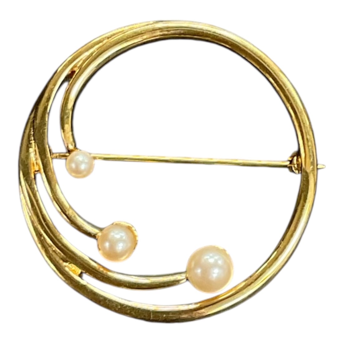 Monet Gold Tone and Faux Pearl Circle Brooch: A gold tone brooch by Monet featuring an open circular design accented with three faux pearl elements along sweeping curved bars. The textured gold tone surface creates contrast with the smooth luster
