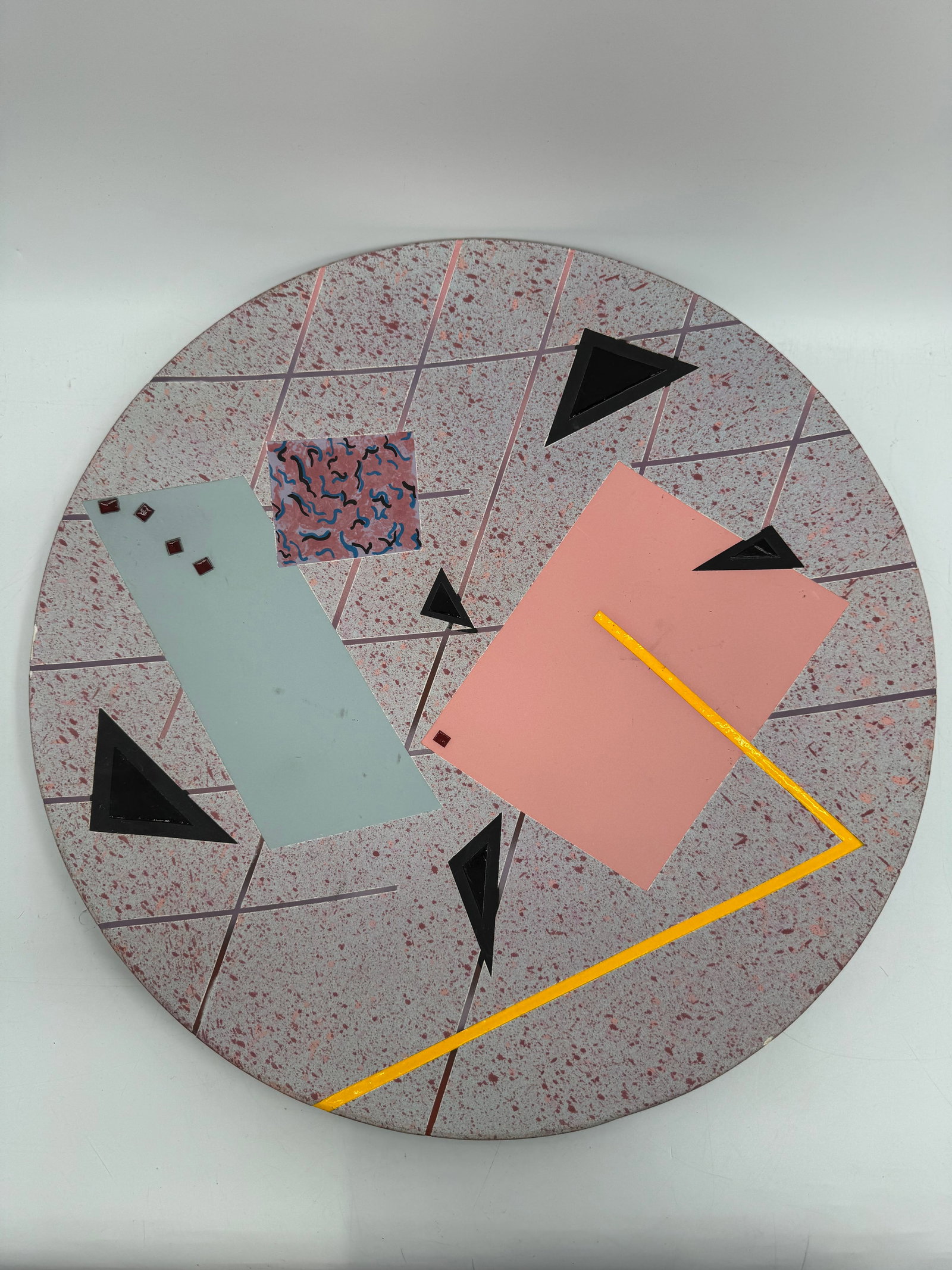 Greg Daly Abstract Geometric Ceramic Wall Plate: Large circular ceramic wall piece by Australian artist Greg Daly, featuring a speckled background with bold geometric shapes in soft pink, teal, black, and yellow. The design showcases Daly’s si