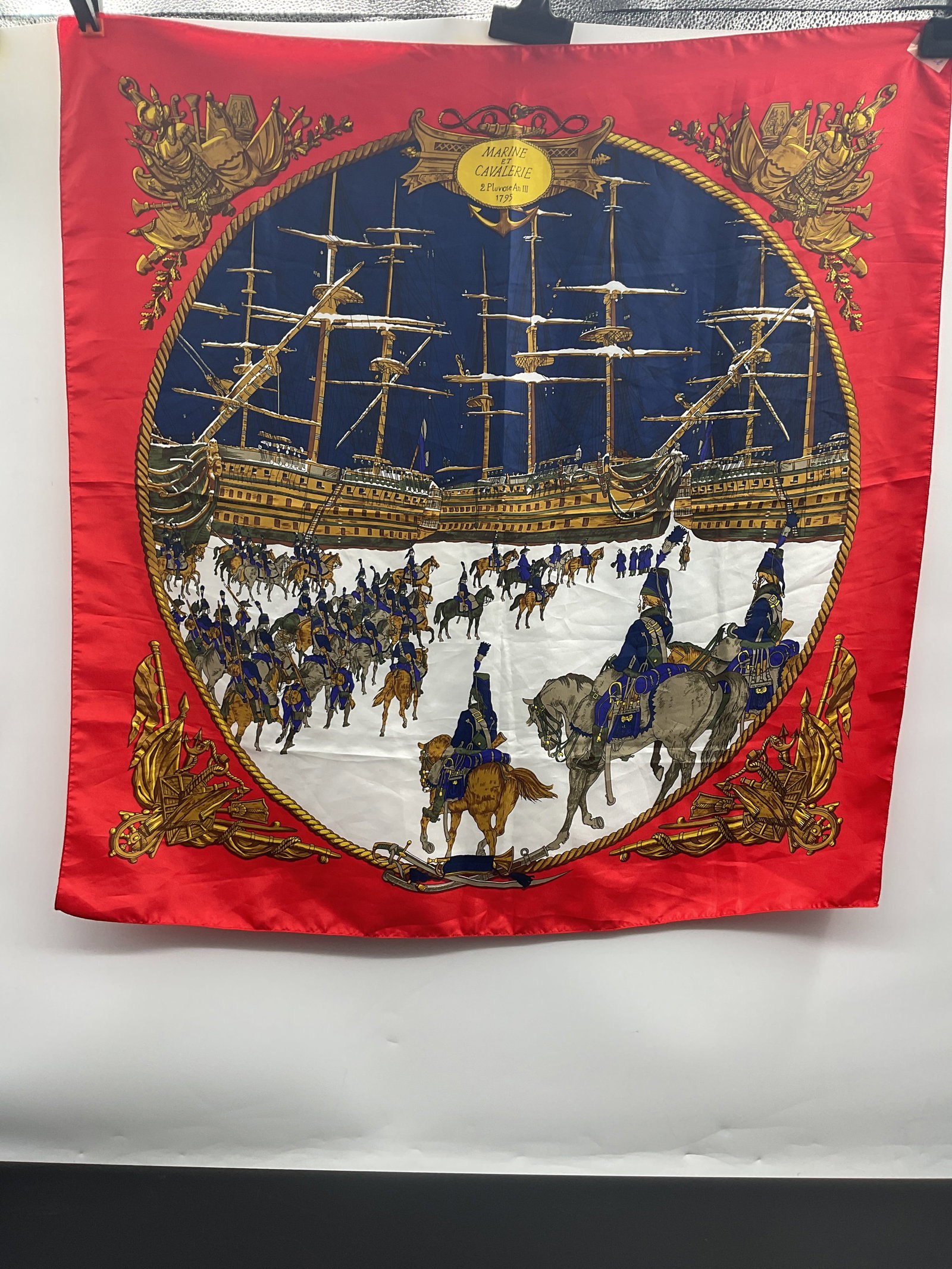 Vintage Silk Scarf with Naval and Equestrian Scene: Vintage silk scarf featuring a detailed design with naval ships and an equestrian procession. The scarf has a red border and measures approximately 35 x 35 inches.
