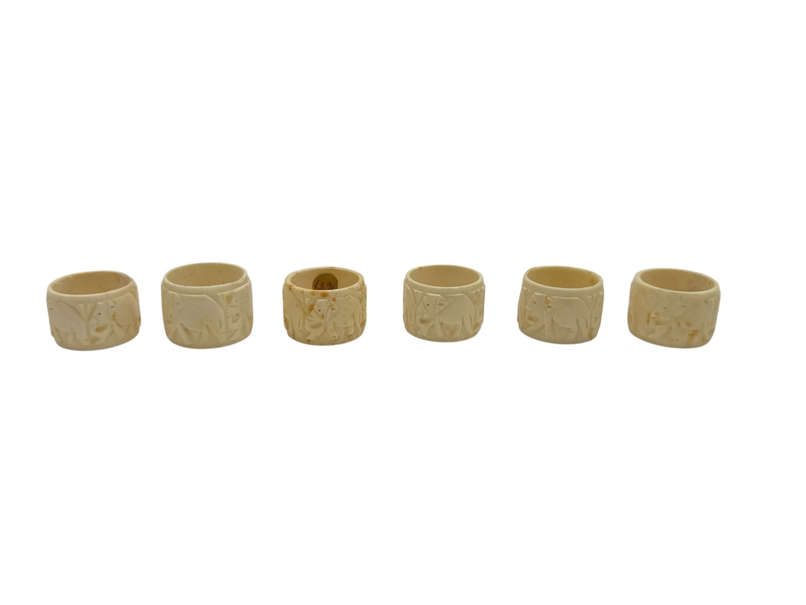 Set of Six Hand-Carved Oriental Figural Napkin Rings, Natural Toned Carved Material: This lot features a finely crafted set of six hand-carved oriental figural napkin rings, each carved in a warm natural tone with detailed relief scenes depicting figures, animals, and traditional moti