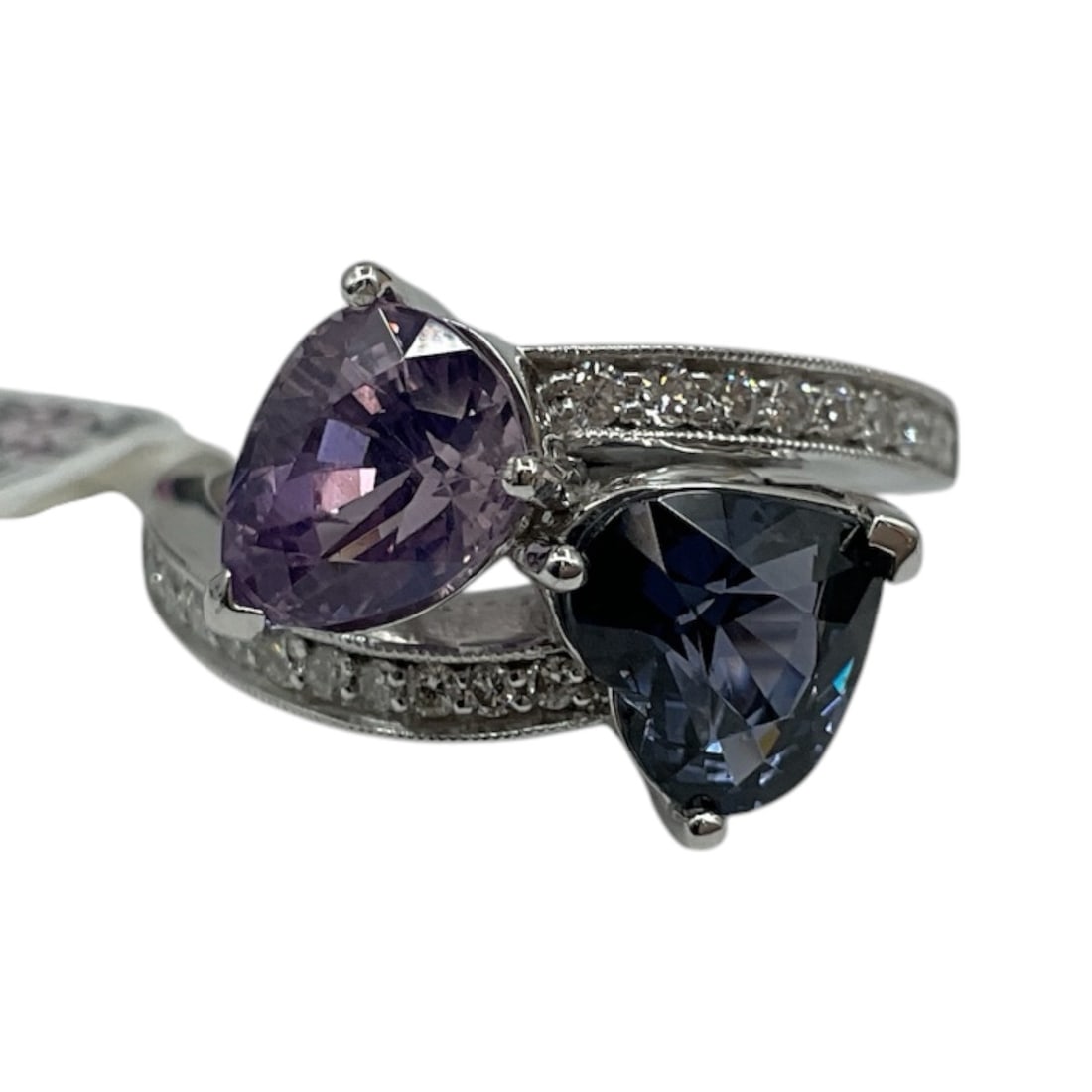 Platinum Multi Sapphire and Diamond Ring with AIGL Appraisal: A striking platinum ring set with two pear-shaped sapphires in contrasting hues—one in a soft lavender tone and the other in a deep blue. The stones are positioned in a bypass design, accented b