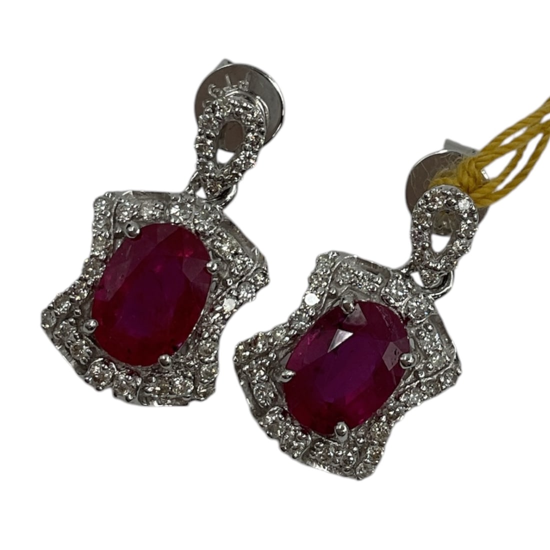 Platinum Ruby and Diamond Drop Earrings with Appraisal: An elegant pair of platinum drop earrings set with vibrant oval-cut rubies, each surrounded by a halo of round brilliant cut diamonds. The earrings feature an articulated design with diamond-set upper