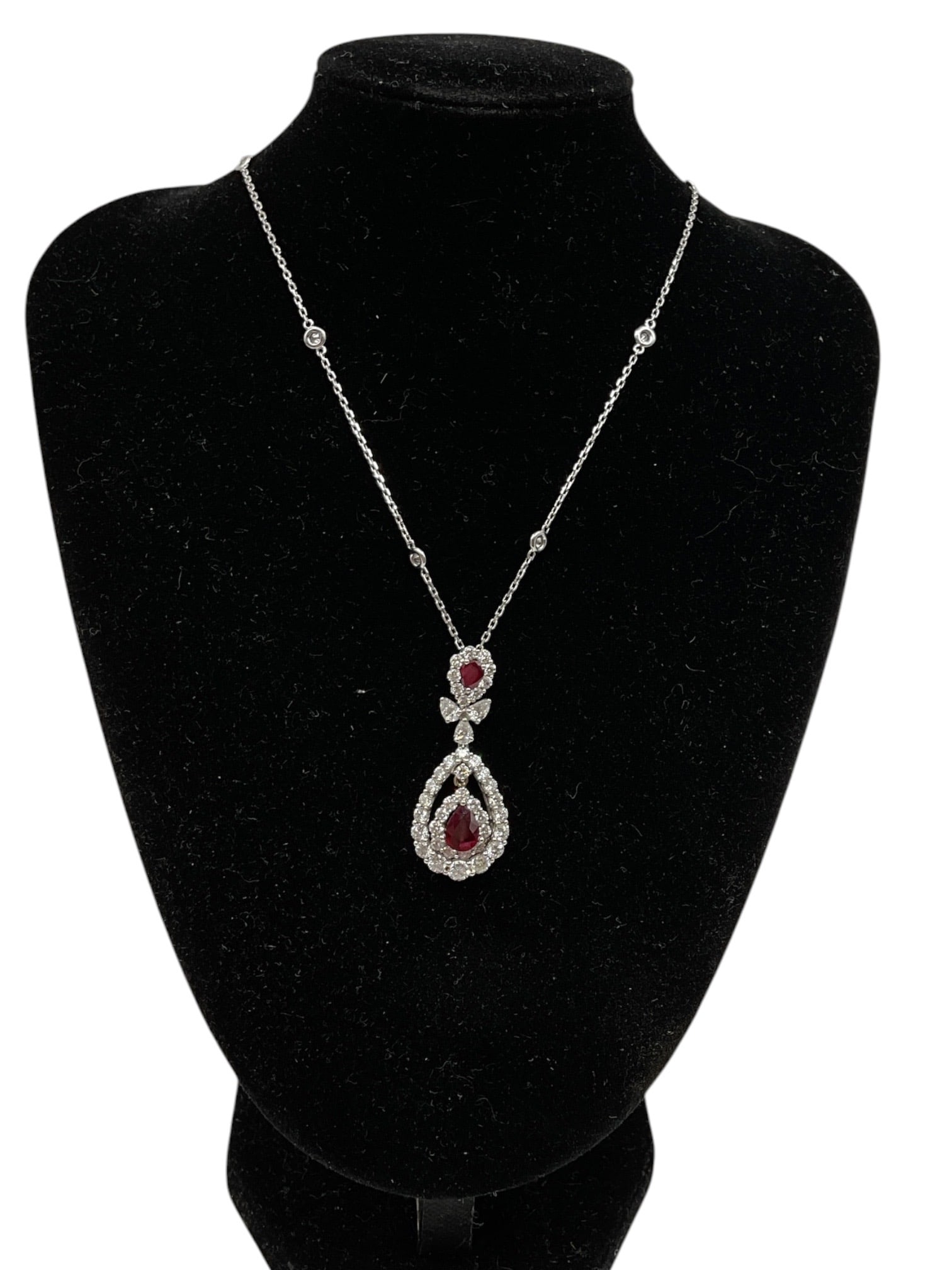 Ruby and Diamond Pendant Necklace: An elegant pendant necklace featuring pear-shaped ruby and diamond drop elements suspended from a delicate chain accented with small diamond stations. The layered openwork pendant design is adorned wi