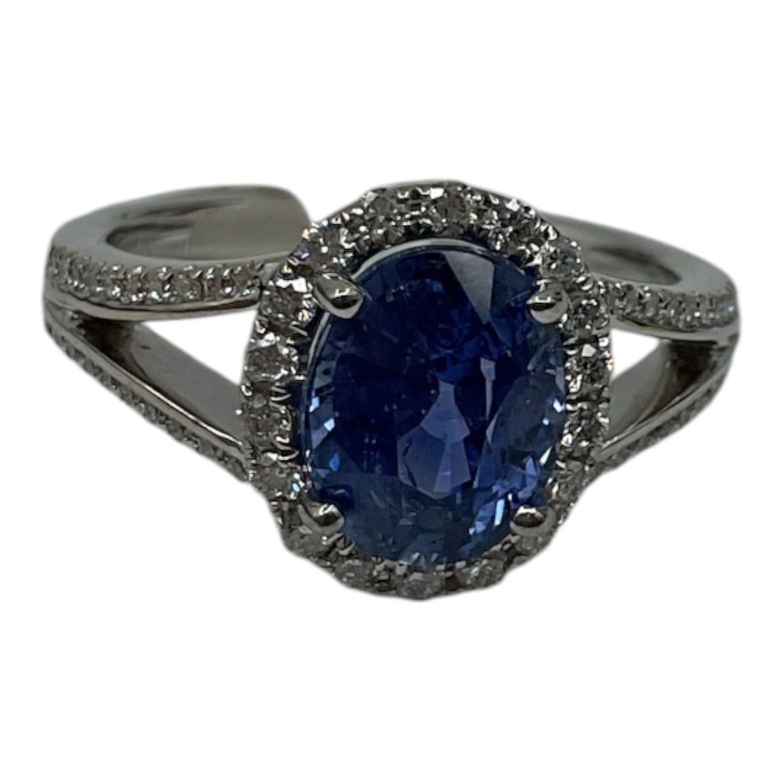 Platinum Sapphire and Diamond Ring with GIA Report: An elegant platinum ring set with a striking oval-cut blue sapphire at center, surrounded by a halo of round brilliant cut diamonds and additional diamonds extending along the split shoulders. The viv