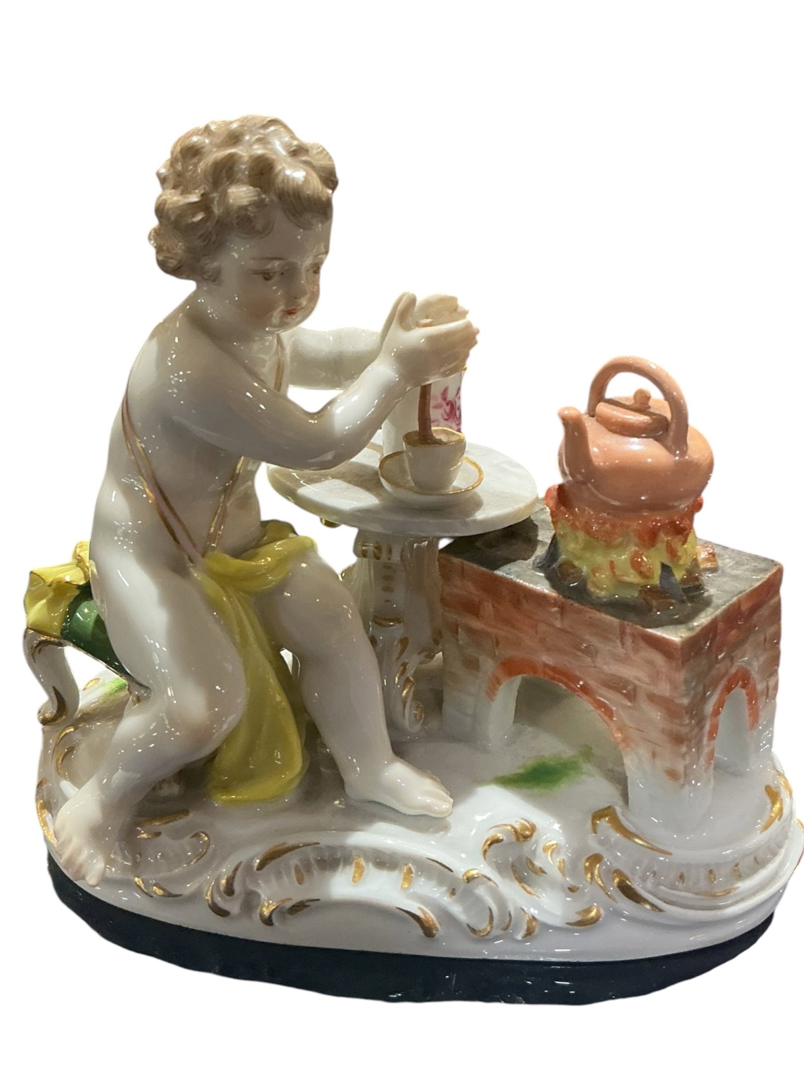 PC573 - 19th Century Meissen Porcelain Cherub Making Drink: A charming 19th century Meissen porcelain figural group depicting a cherub engaged in a domestic scene, seated at a small table preparing a drink. This delightful composition reflects the playful and 