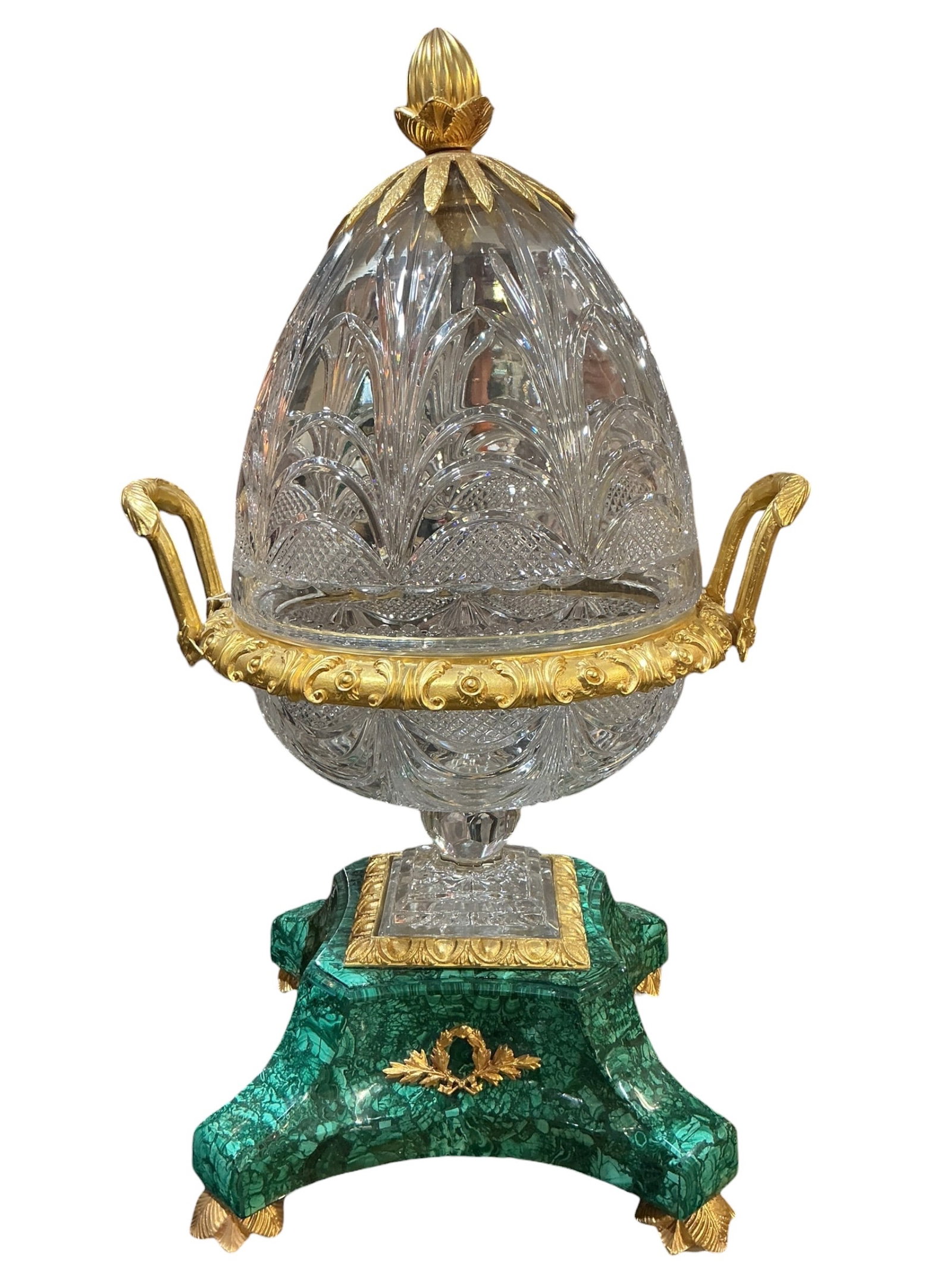 CS374- Crystal and Dore Bronze Mounted Egg on Malachite Base: A finely crafted decorative object featuring a cut crystal egg mounted in dore bronze and set upon a richly patterned malachite base. The egg form is intricately cut with detailed geometric and foliat