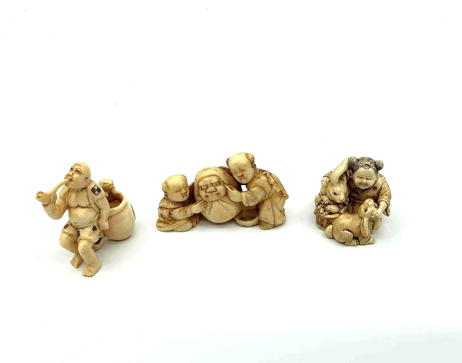 Three Japanese Style Netsuke Figurines: Group of intricately carved figures including a pair of joyful characters with a drum a seated figure holding an object and a cluster of figures possibly depicting a family scene likely crafted from r
