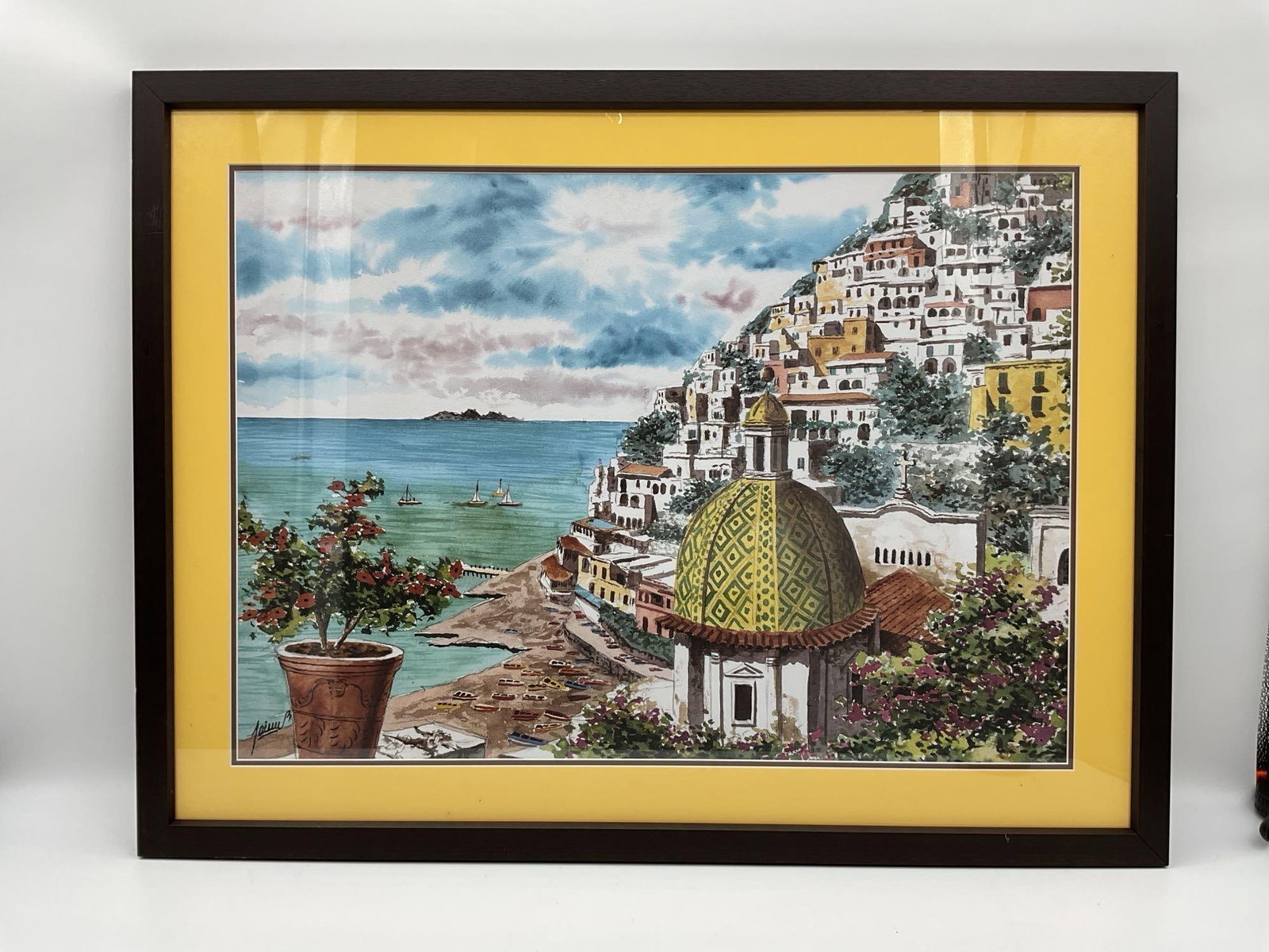 Positano Coastline with Dome: Framed watercolor-style print of Positano, Italy, depicting the iconic dome of the Church of Santa Maria Assunta, a hillside of pastel buildings, and sailboats dotting the turquoise sea. A potted plan