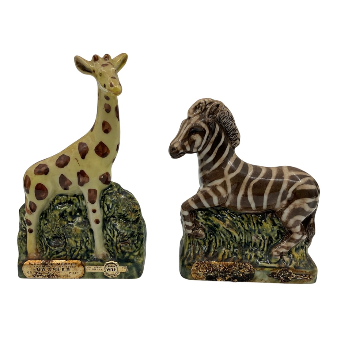 Vintage Garnier Giraffe and Zebra Porcelain Liquor Decanter Bottles 1973: Charming pair of vintage Garnier collectible liquor decanters from 1973, modeled as a giraffe and zebra standing against textured green foliage bases. Each figural bottle is crafted in glazed ceramic