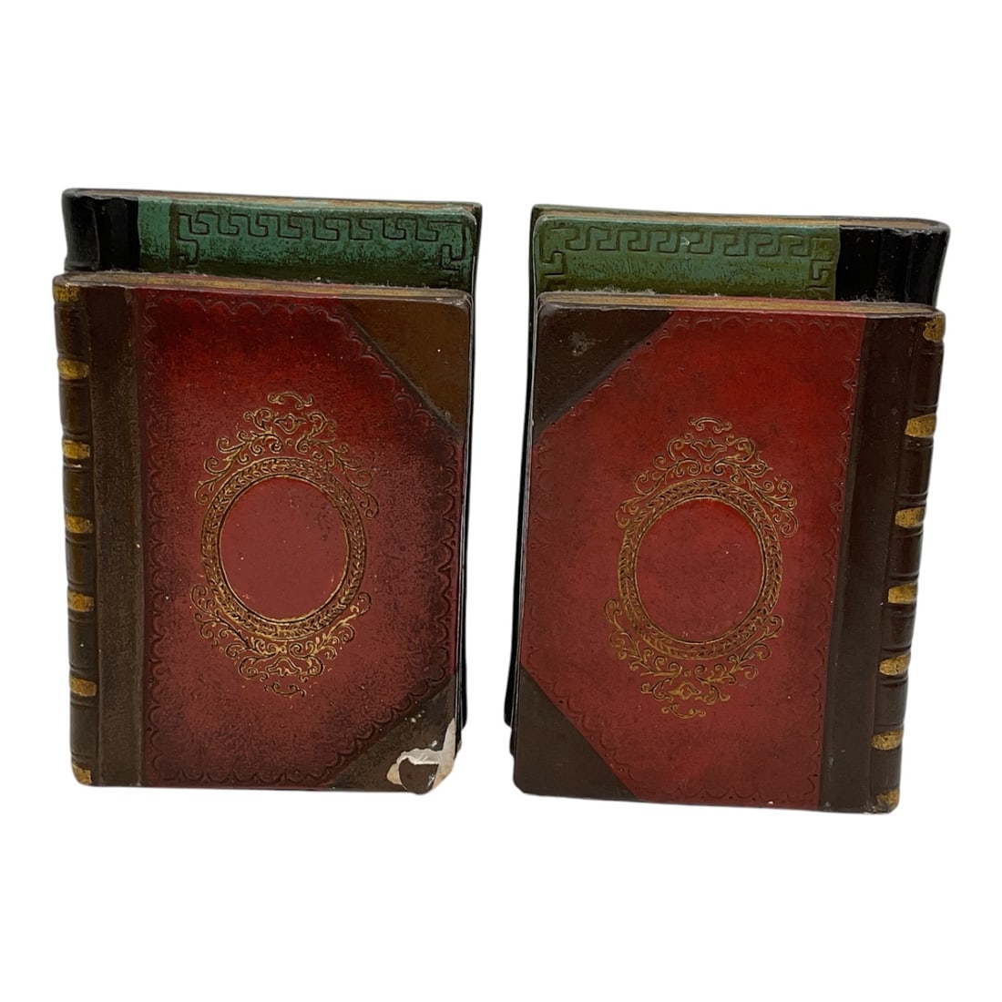 Pair of Faux Book Form Metal Bookends: Decorative pair of metal bookends designed in the form of antique leather-bound books with embossed gilt style decoration and simulated spines. Features painted red, brown, and black finishes with