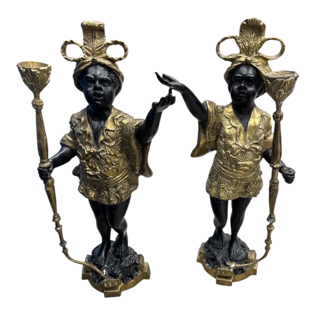 Pair of Decorative Blackamoor Style Figural Candle Holders with Gilt Accents: Striking pair of decorative figural candle holders in the Blackamoor style, featuring standing figures dressed in gilt patterned attire and holding tall torch-form candle sconces. Finished in