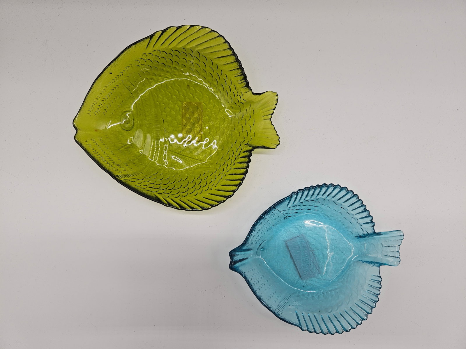Two Vintage Fish-Shaped Glass Dishes: Two vintage glass dishes in the shape of fish, one blue and one green. Blue dish dimensions: H: 1in, W: 7in, L: 5in. Green dish dimensions: H: 2in, W: 8in, L: 7in.