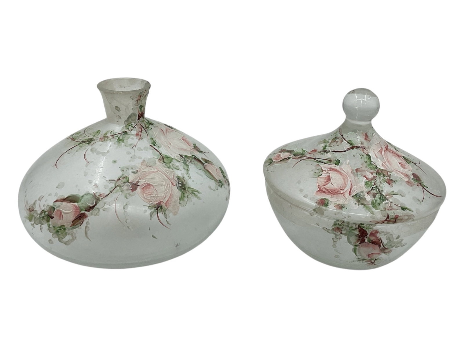 Pair of Hand Painted Frosted Glass Floral Dresser Jars: Decorative pair of frosted glass dresser jars featuring hand painted floral decoration with pink roses and trailing greenery. Includes one bottle-form vessel and one covered powder jar with matching f