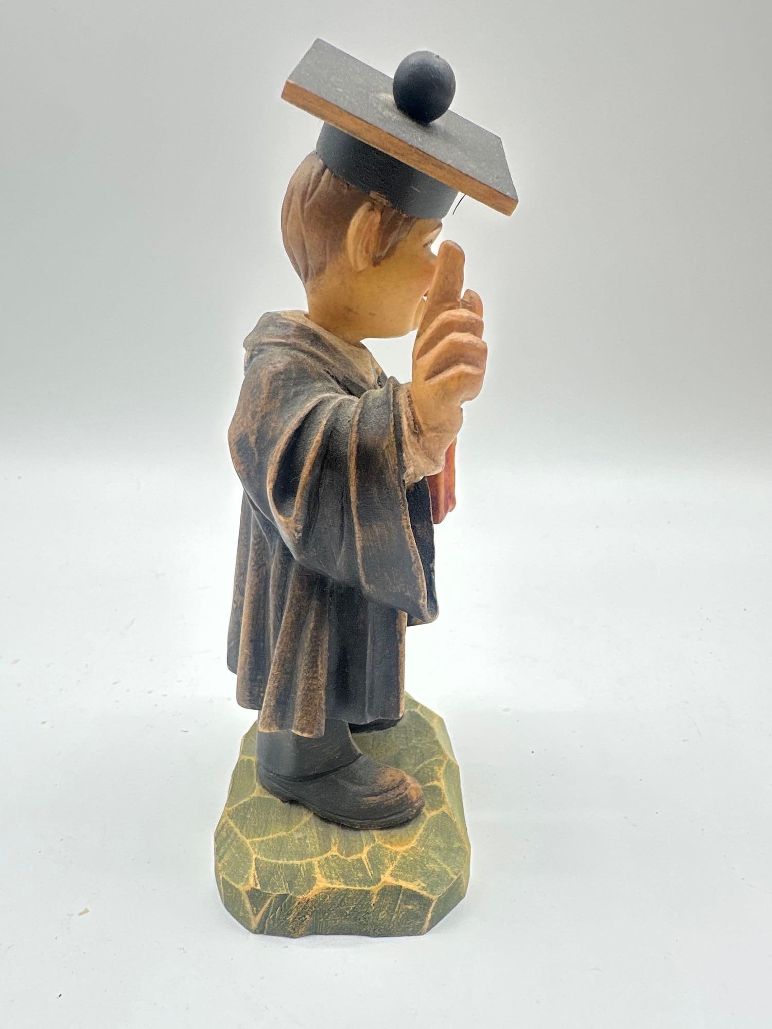 Graduation Professor Anri Figurine - Val Gardena, Italy: Hand-carved and painted wooden figure of a smiling professor or scholar in academic robes and cap, holding a book and raising one finger as if making a point. Medium: painted wood 3x2x7”